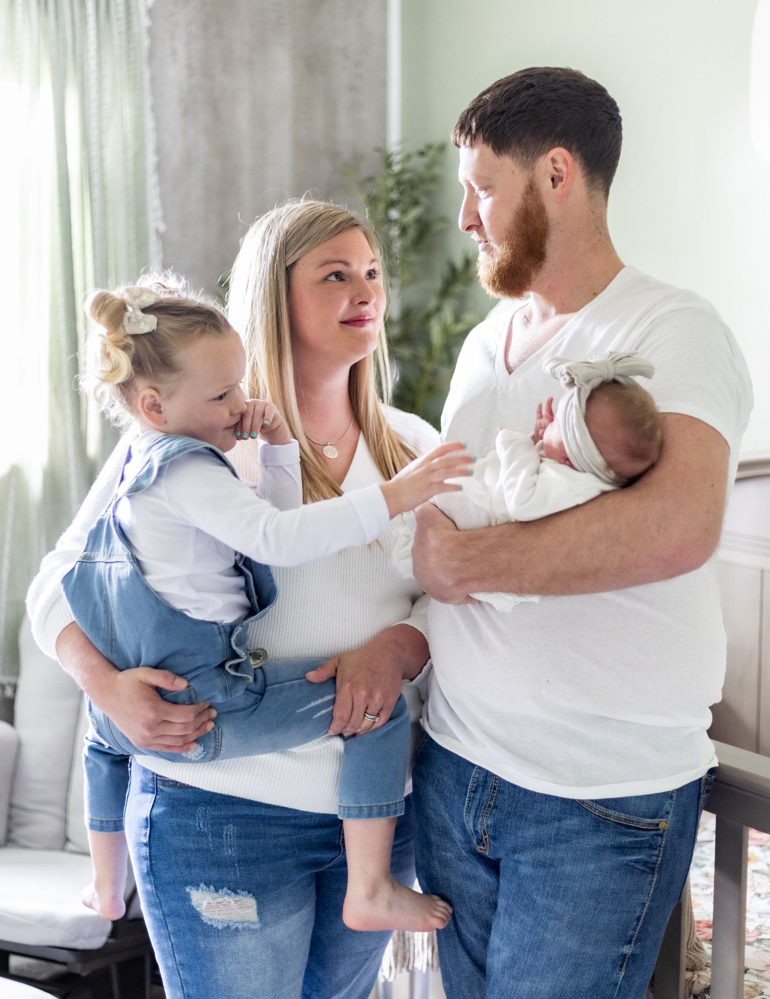 A family in matching white tops and jeans embraces while standing together in a bright room. Cincinnati/ Northern Kentucky