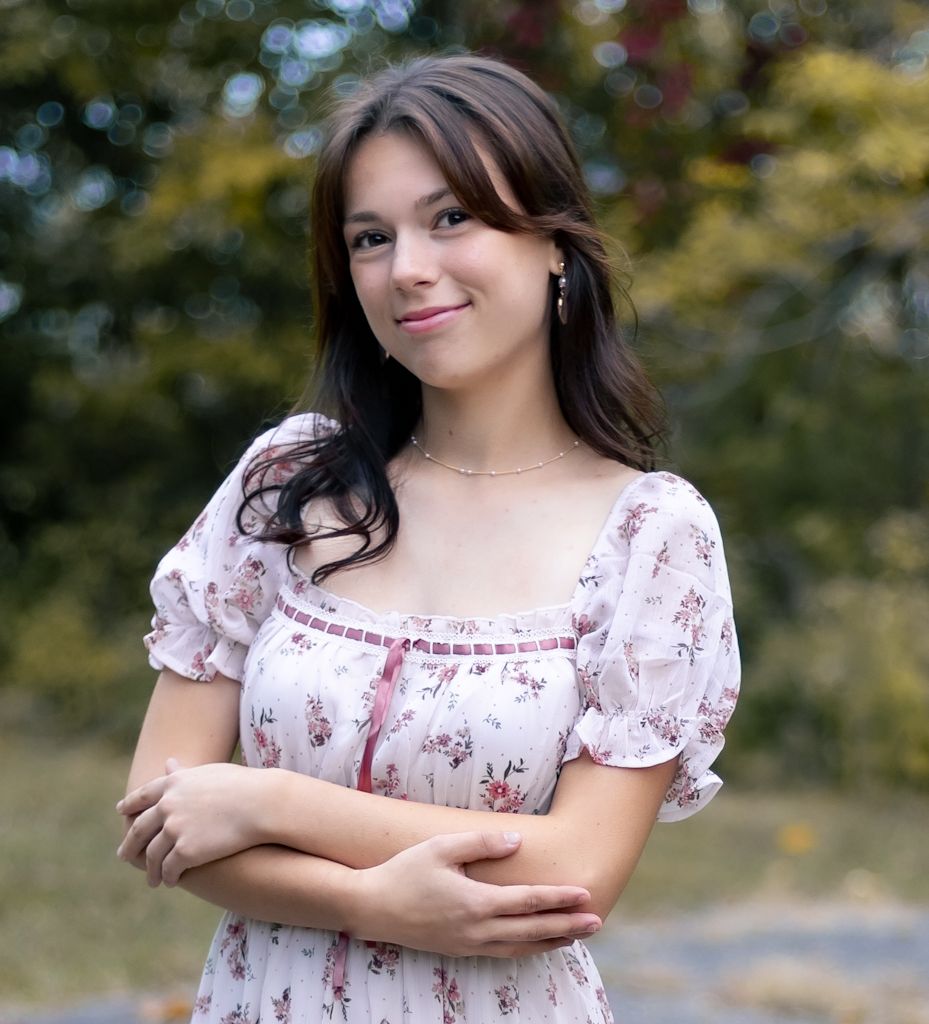 A woman in a floral print dress with puff sleeves stands outdoors with crossed arms and a warm smile. Cincinnati/ northern Kentucky