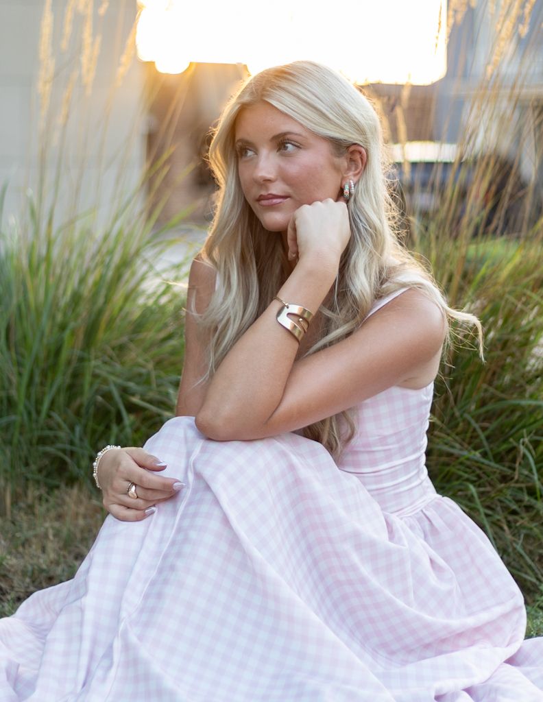 A photo showing a person in a white gingham dress sitting thoughtfully in tall grass at sunset. Cincinnati/ northern Kentucky