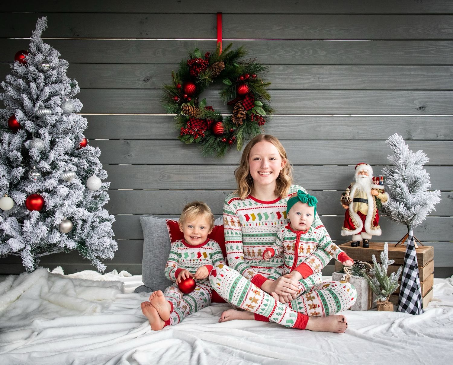 A festive Christmas photo showing people in matching holiday pajamas posing against a gray wooden wall with decorations.