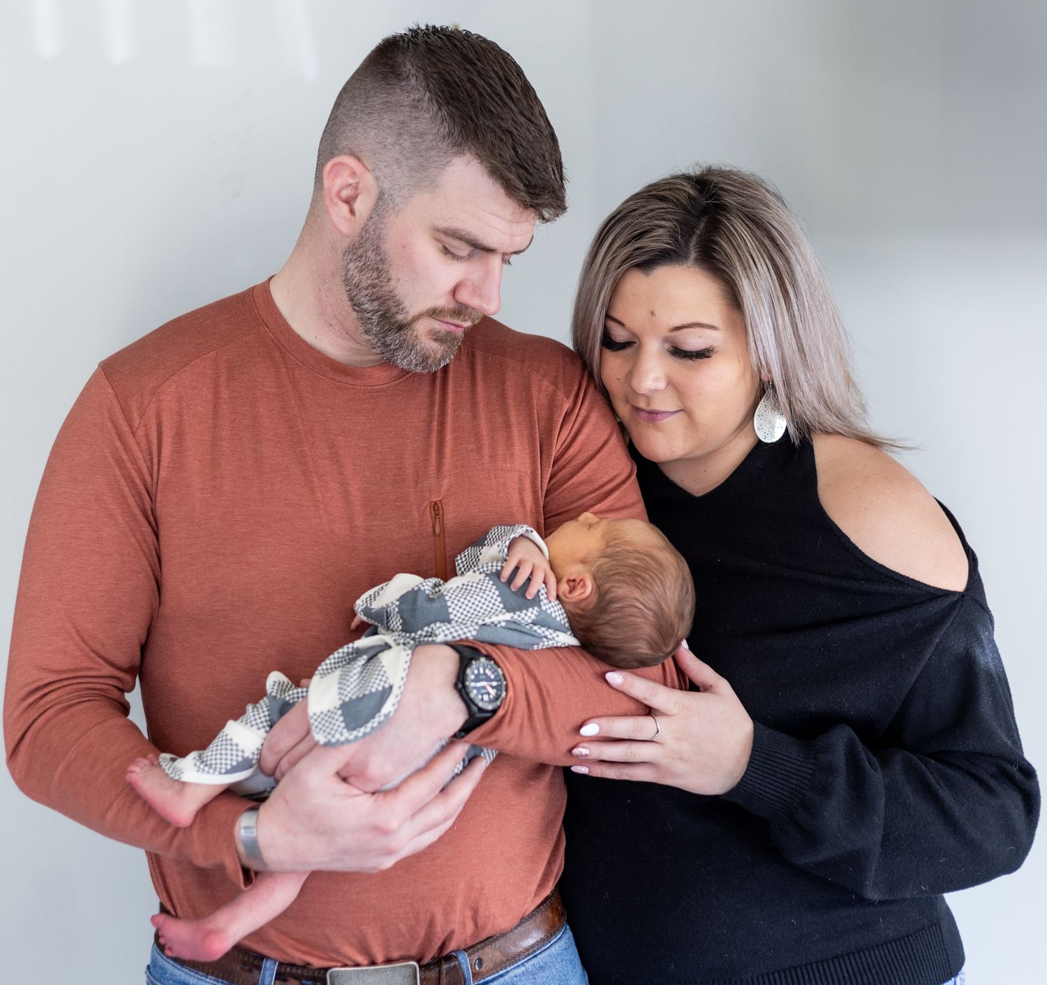 A couple in a rust-colored sweater and navy top share tender moments with their newborn baby in a photo series. Cincinnati/ Northern Kentuck