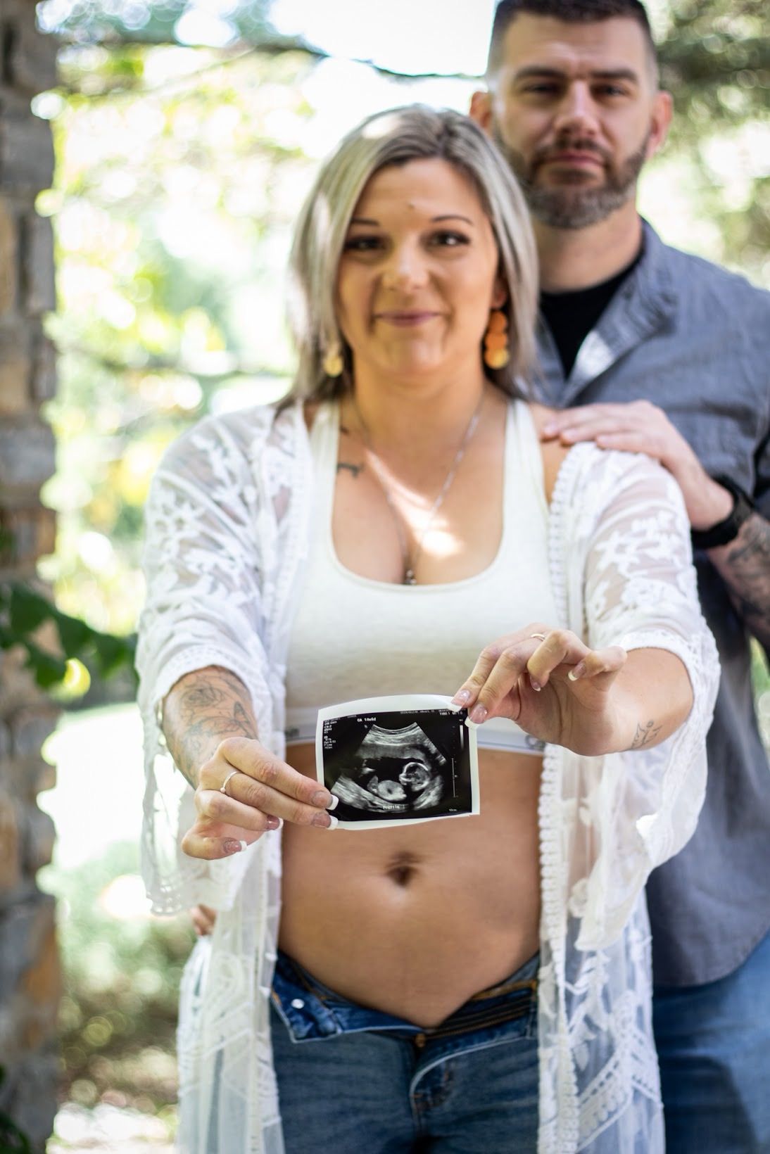 A pregnancy announcement photo series shows a couple holding ultrasound images while standing outdoors in natural lighting. Cincinnati