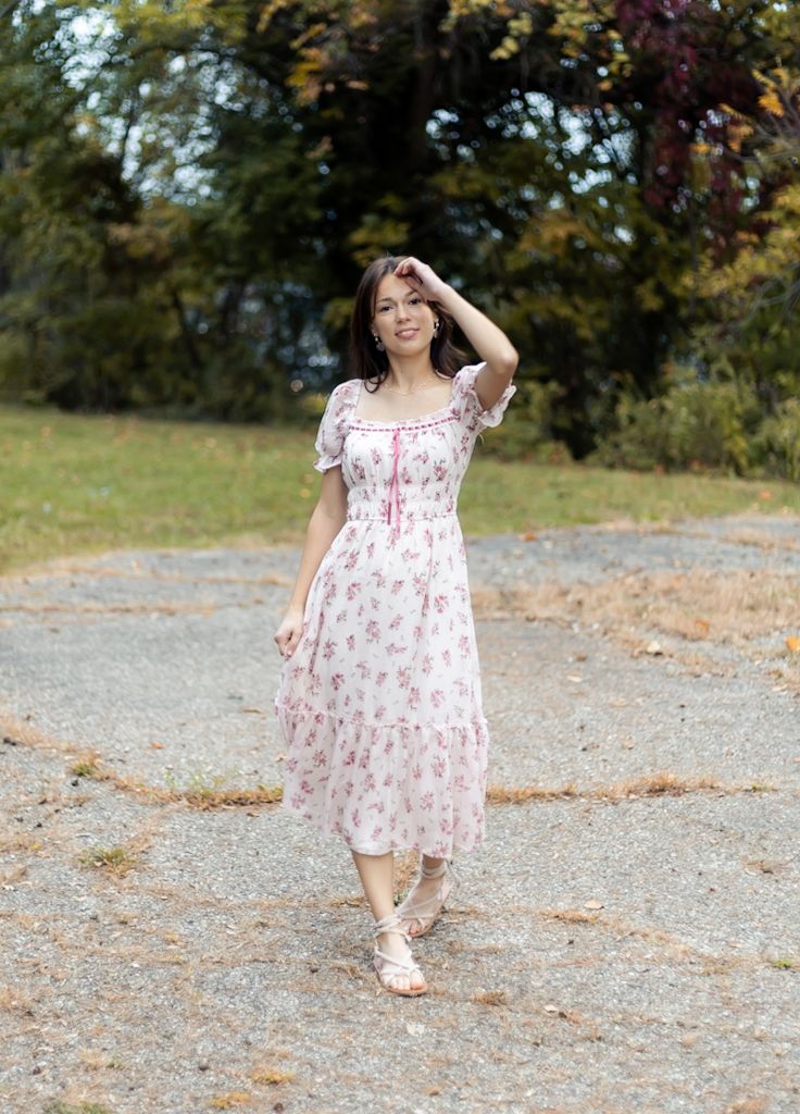 A person in a floral print dress twirls playfully on a gravel path surrounded by autumn trees. Cincinnati/ northern Kentucky