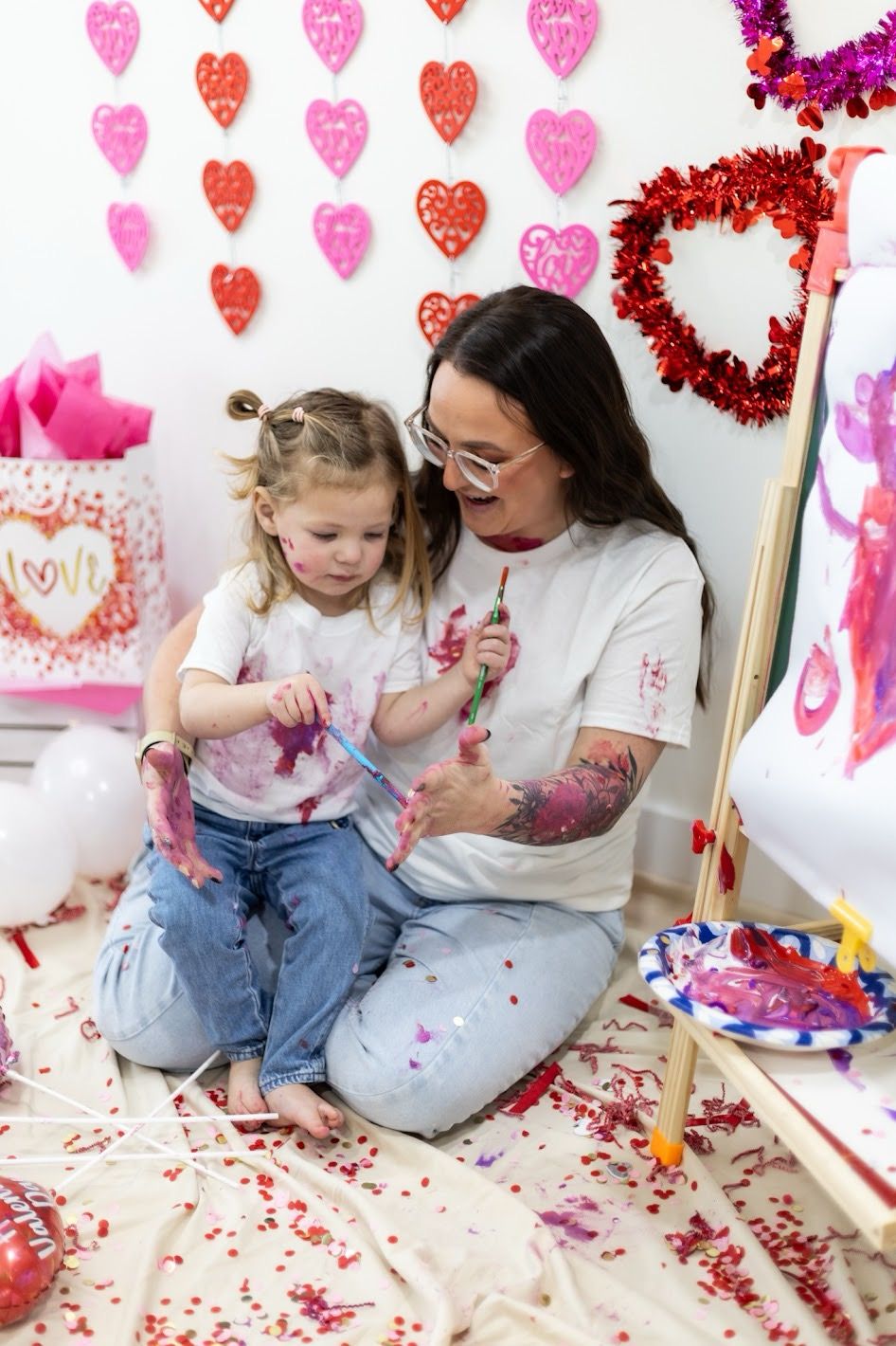 Parent and child sit together on floor surrounded by Valentine's Day decorations and pink heart shapes. Cincinnati/ northern Kentucky