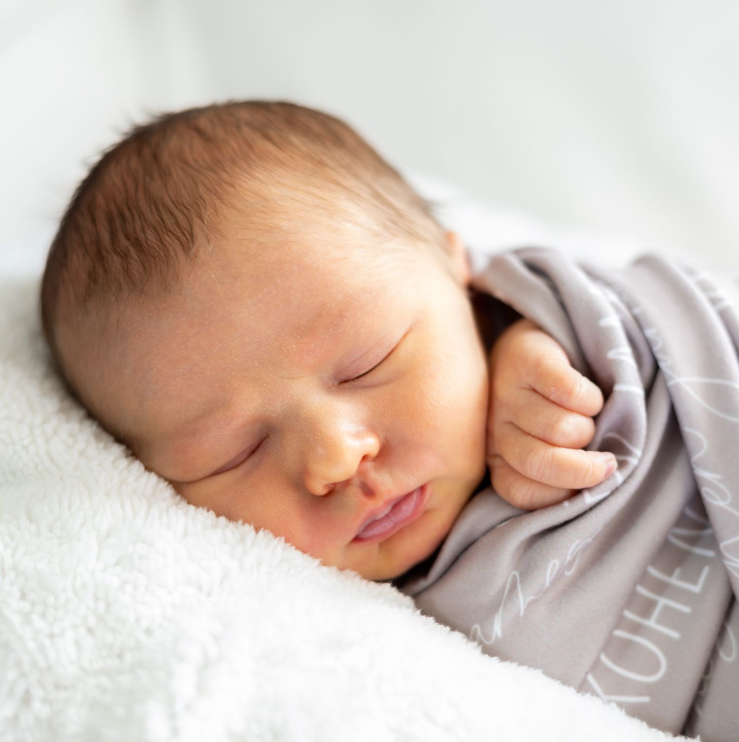 Sleeping newborn baby in gray onesie lying on soft white blanket in peaceful slumber. Cincinnati/ Northern Kentucky