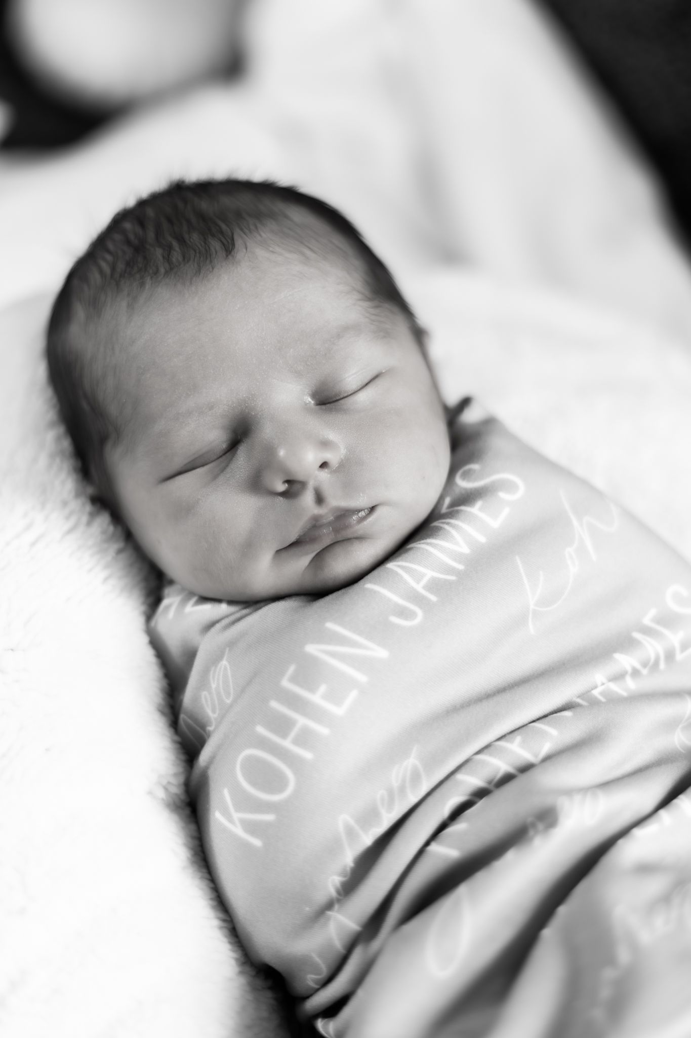 A sleeping baby wearing grey clothing rests peacefully on white bedding. Cincinnati/ Northern Kentucky