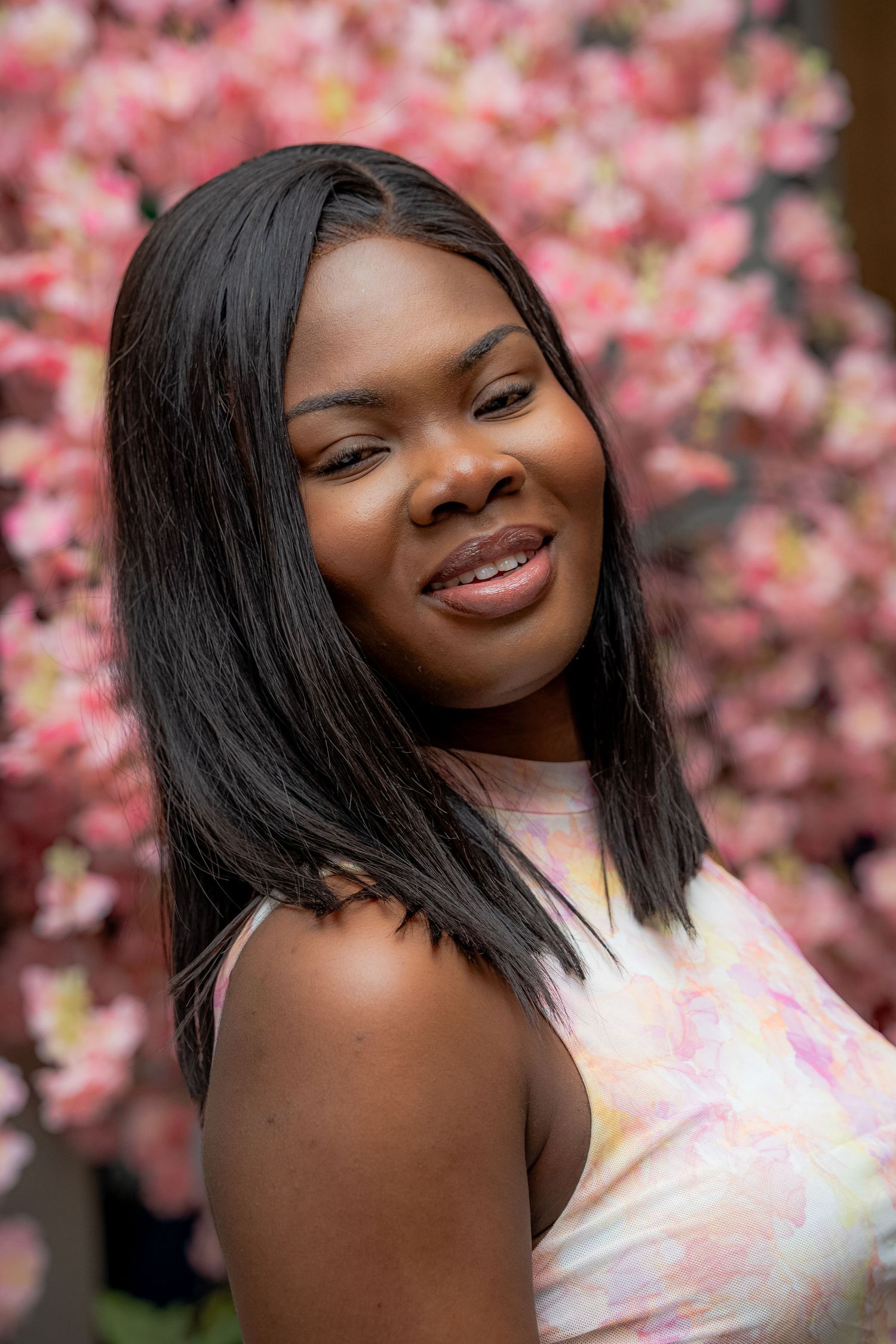 Portrait in front of pink cherry blossoms with a joyful smile wearing a pastel patterned top.