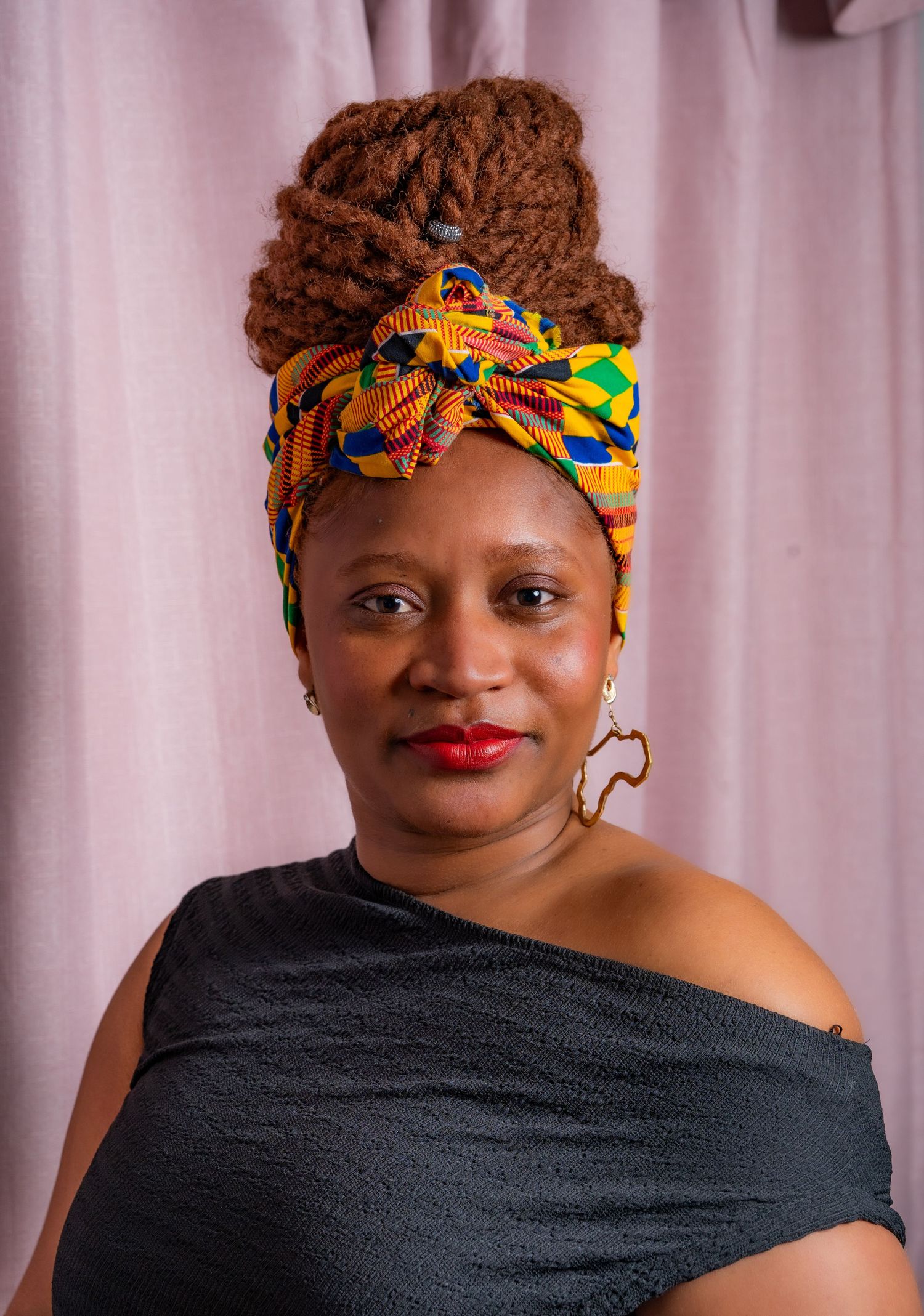Portrait showing vibrant African print headwrap in yellow and blue against black off-shoulder top with red lipstick.