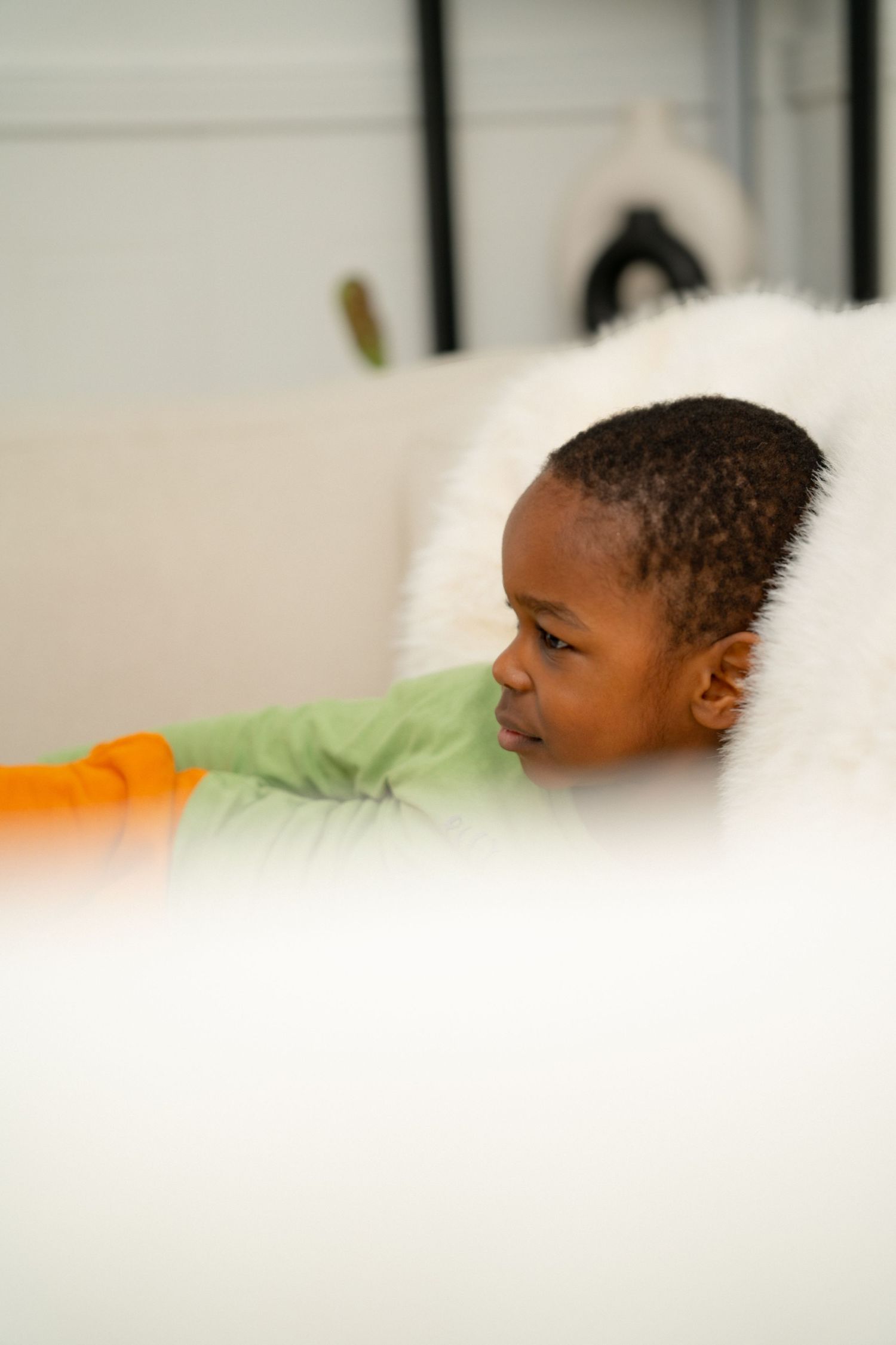 A young child rests peacefully against soft white pillows while wearing an orange and green outfit.