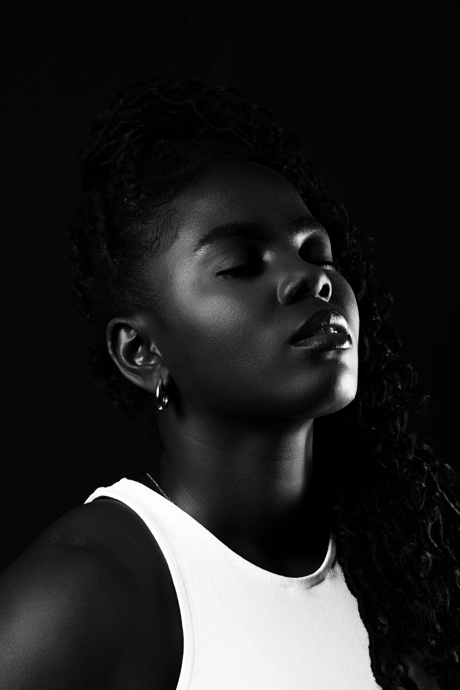 A dramatic black and white portrait showcasing strong contrast with a delicate side-lit composition with natural curls.