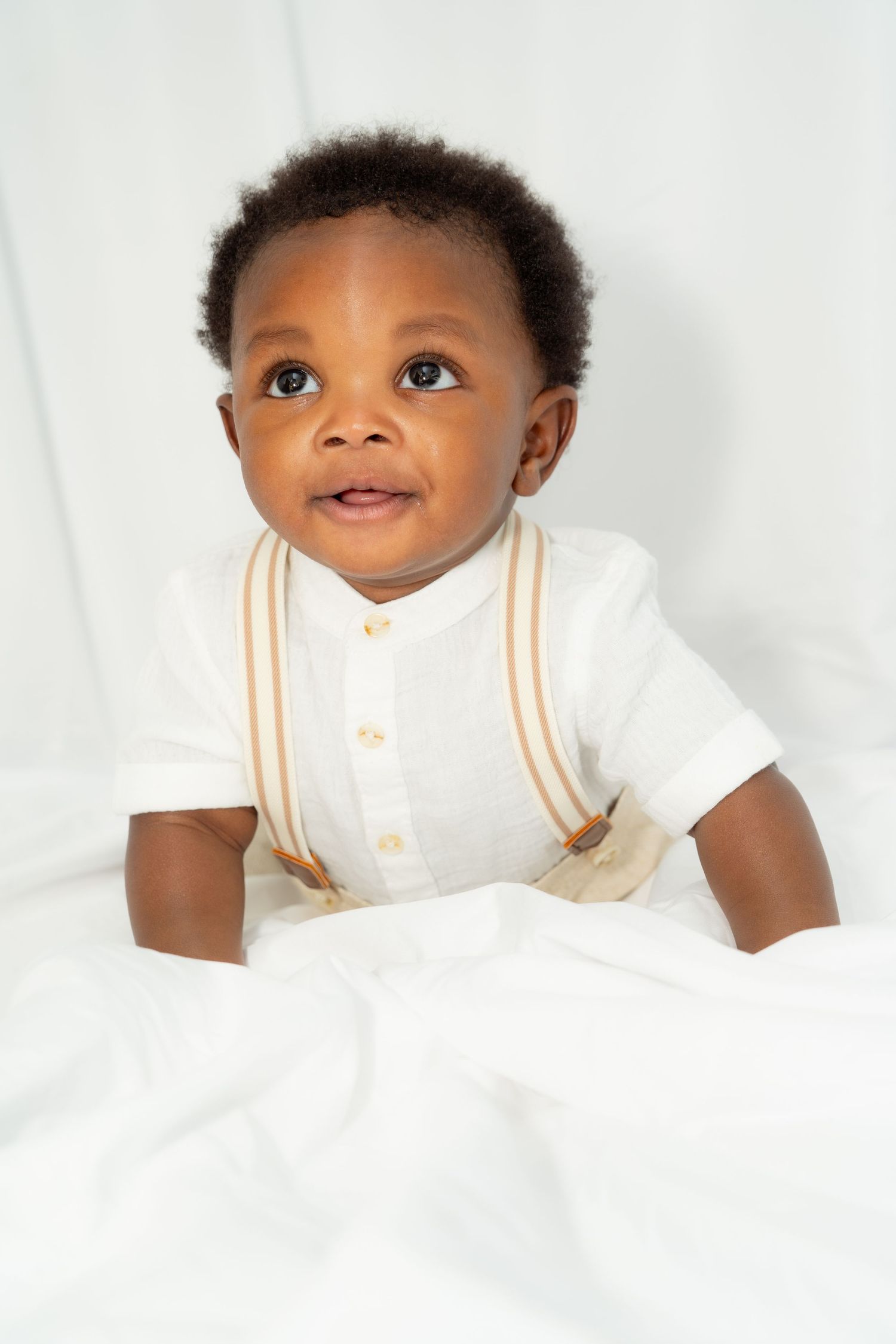 Happy infant in a white button-up shirt with tan stripes sits against a white backdrop.