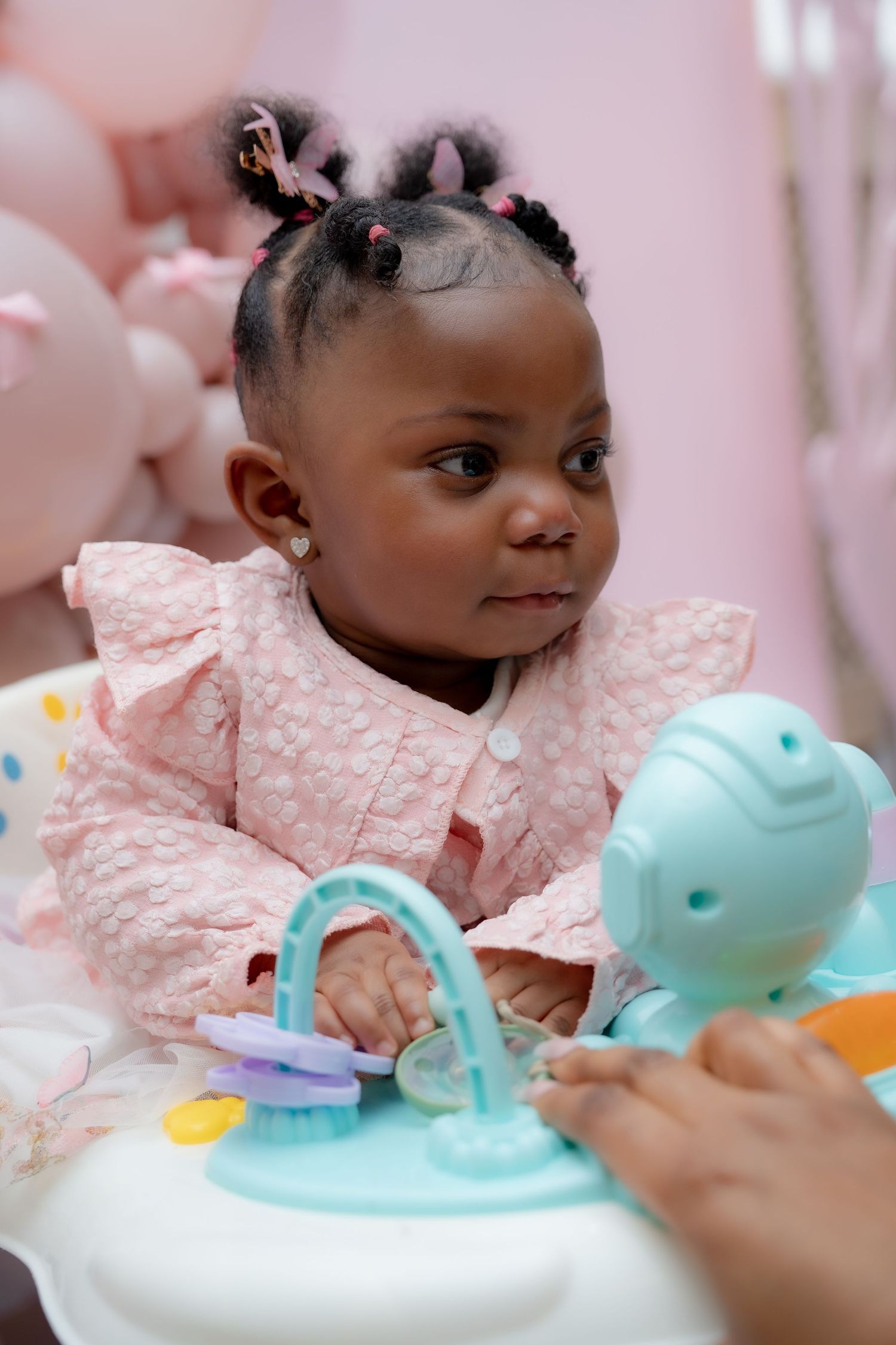 Small child in pink lace dress plays with colorful toys during playtime against pink background.