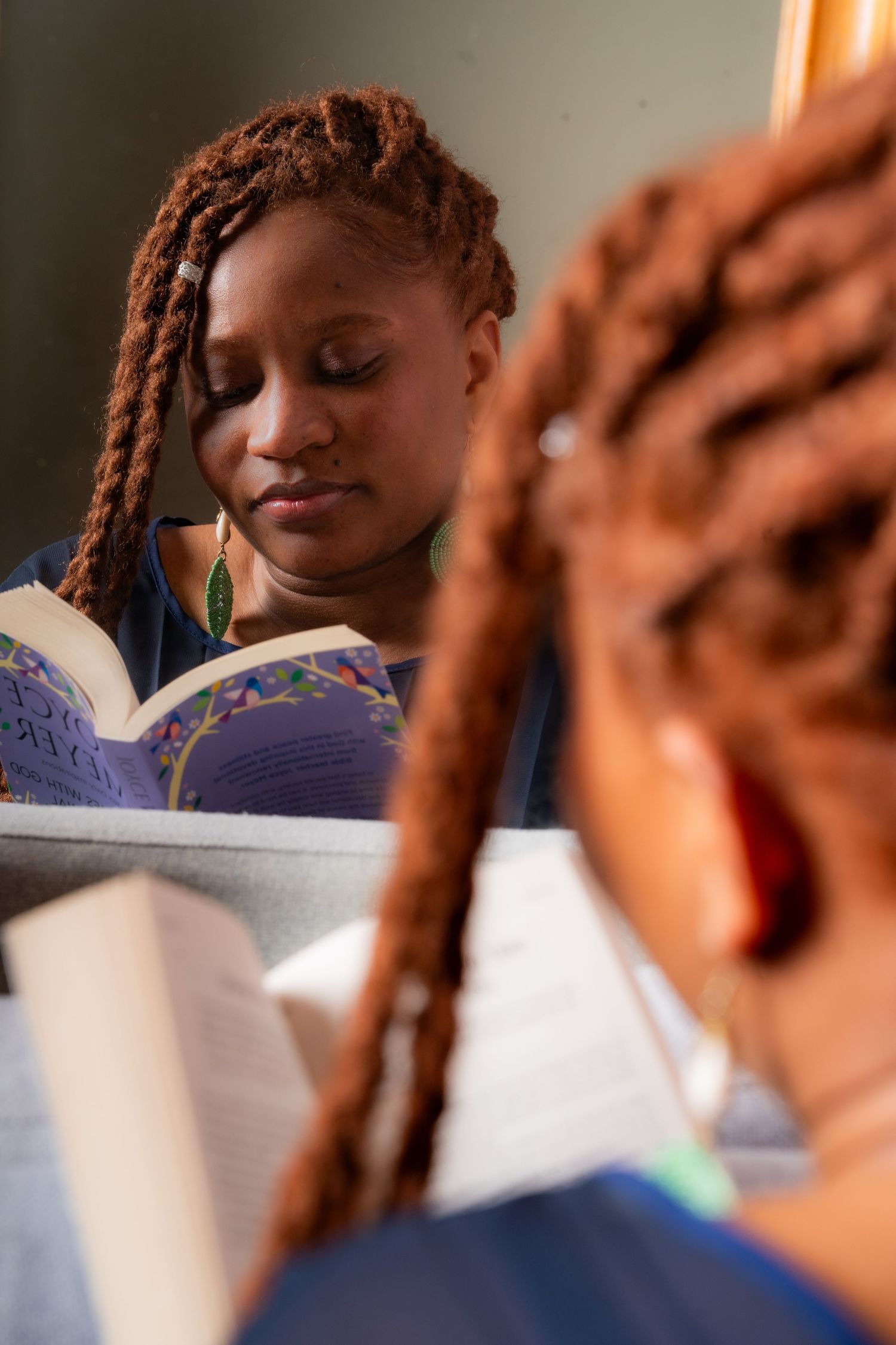 Reader enjoying a book with braided hair and gold earrings in warm lighting.