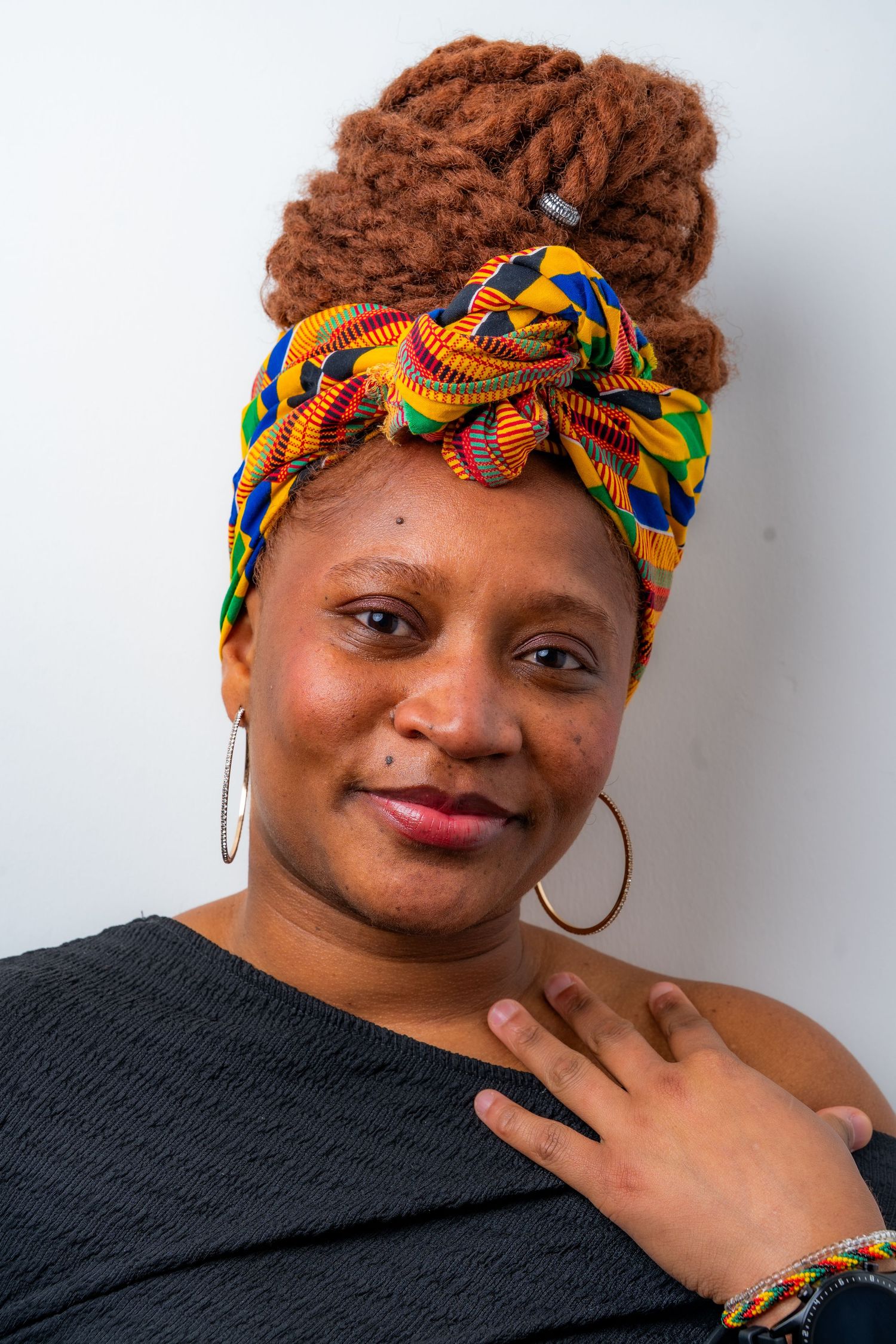 Portrait of someone wearing a vibrant African print headwrap and black top against white background.