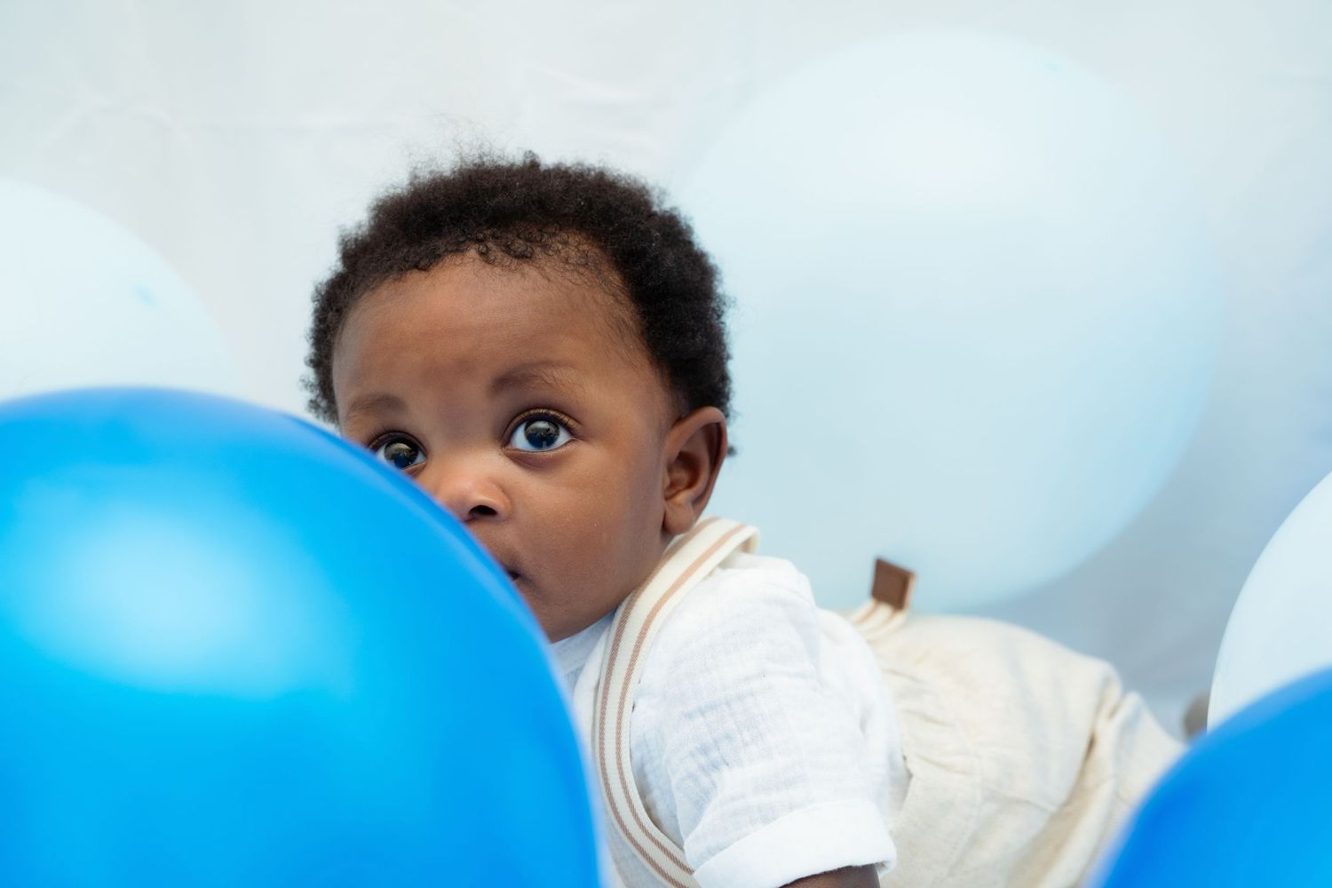 Small child peeks over a bright blue balloon against a light background.