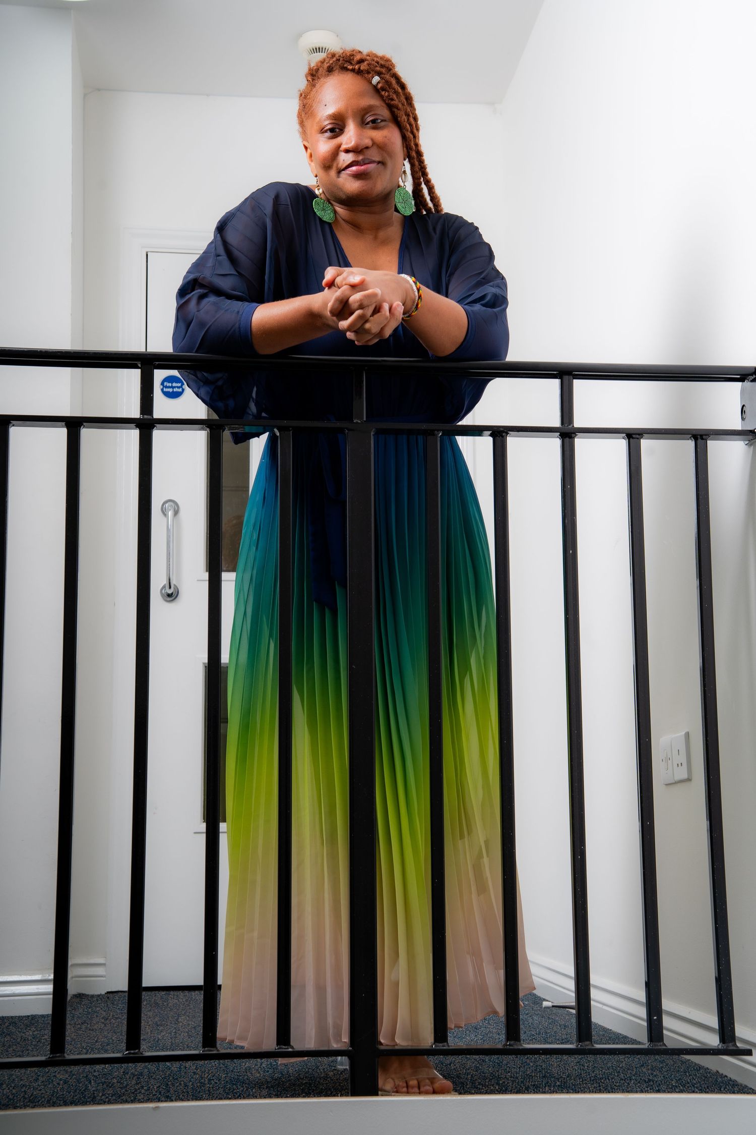 Someone wearing a navy top and stunning gradient maxi skirt in teal, lime green and beige poses against a railing.