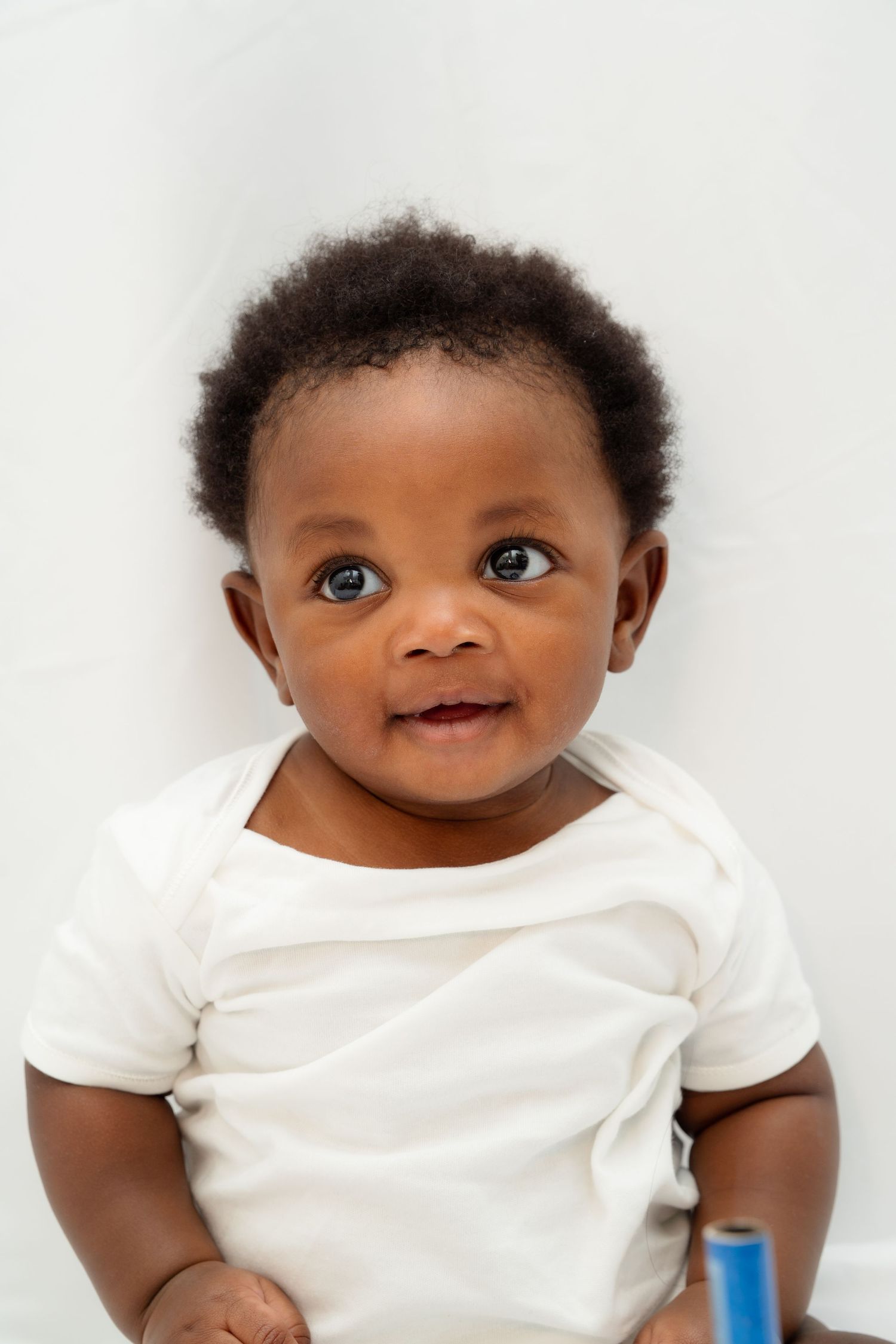Adorable baby in white t-shirt smiles with bright eyes against white background.