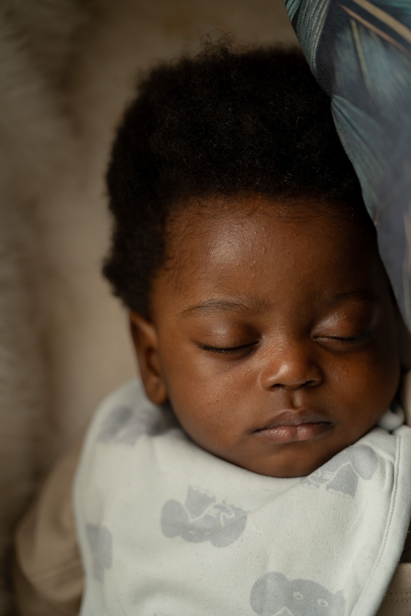 A peaceful sleeping child in a white patterned onesie rests with closed eyes in soft lighting.