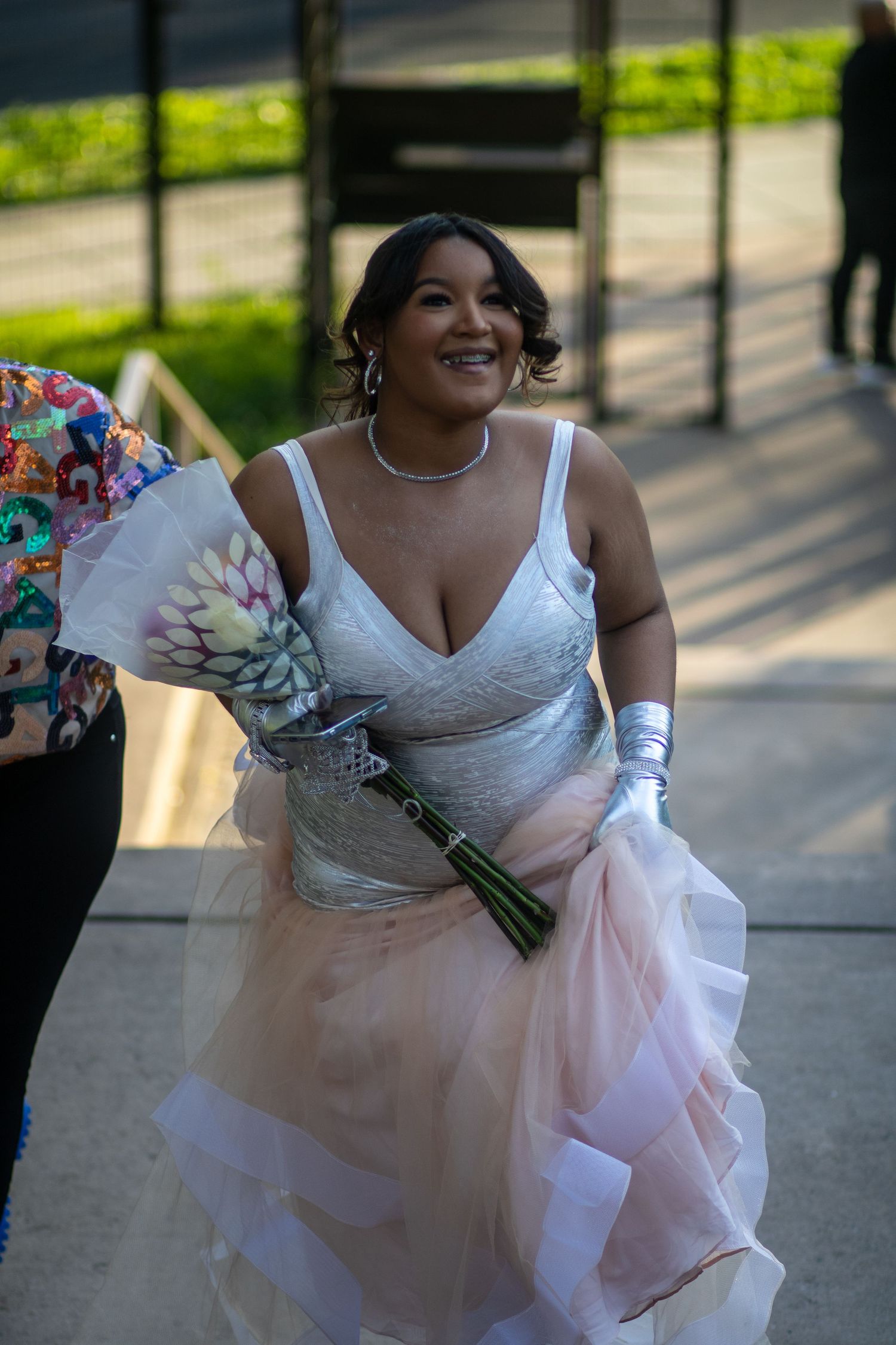 A bride holding a bouquet smiles while wearing a beautiful white wedding dress outdoors.