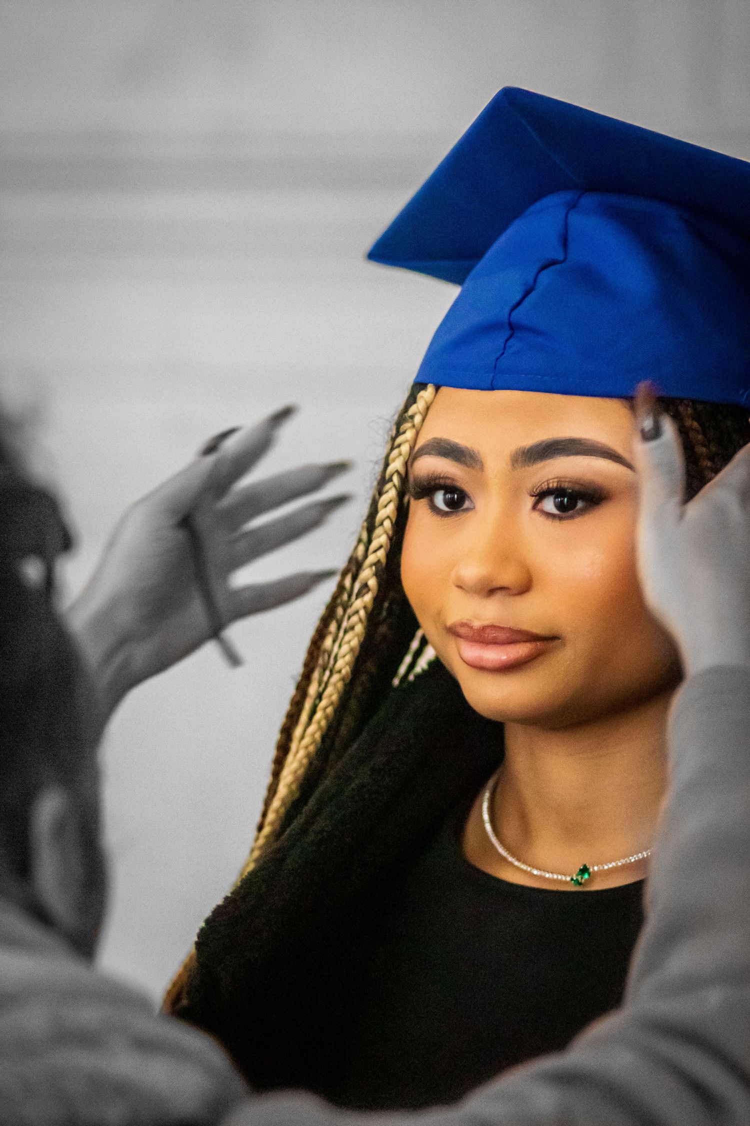 Graduate in blue cap with braids and elegant makeup poses for portrait photo.