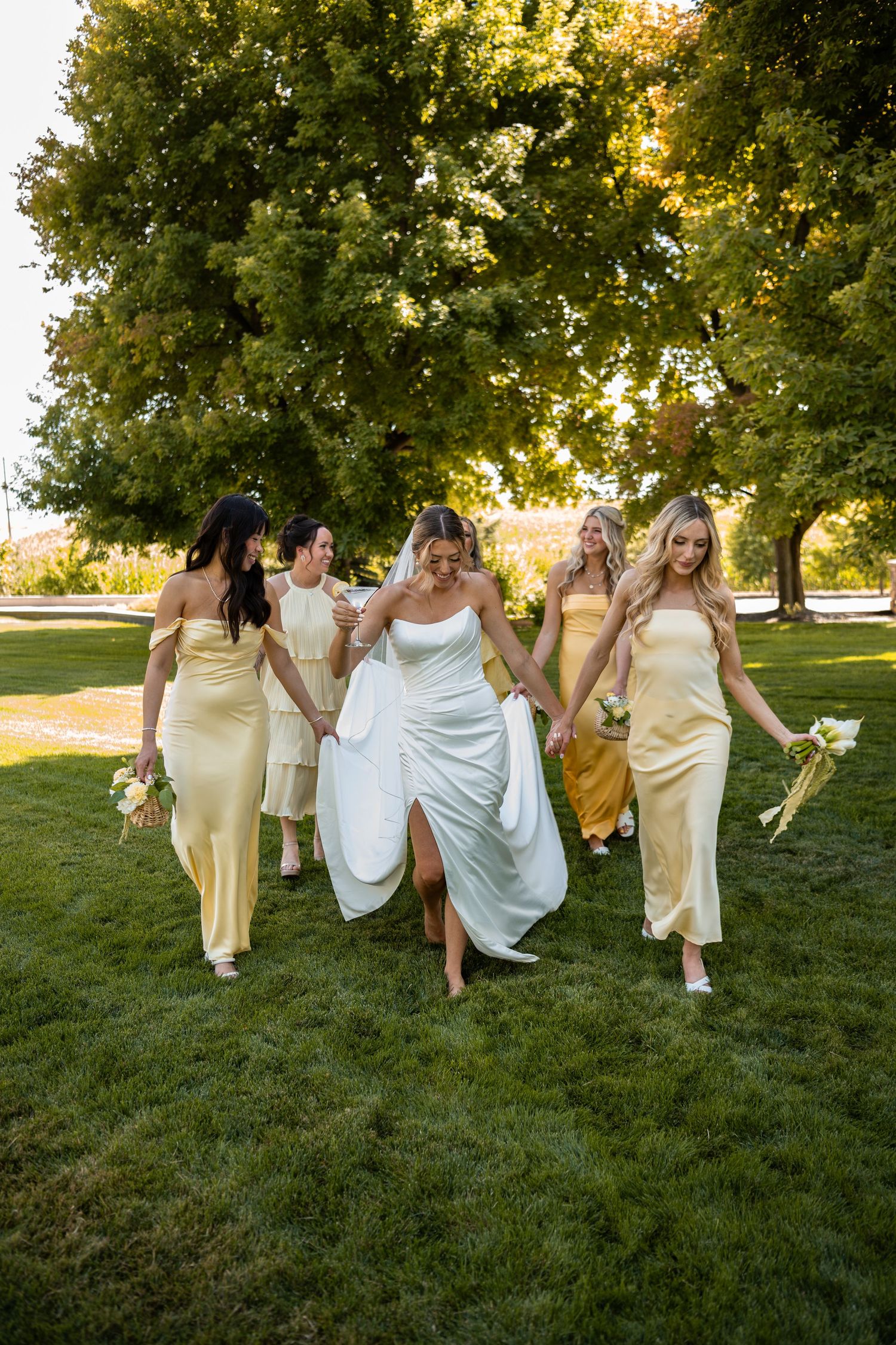 Group in yellow and white dresses walking and laughing together on a grassy lawn at sunset.