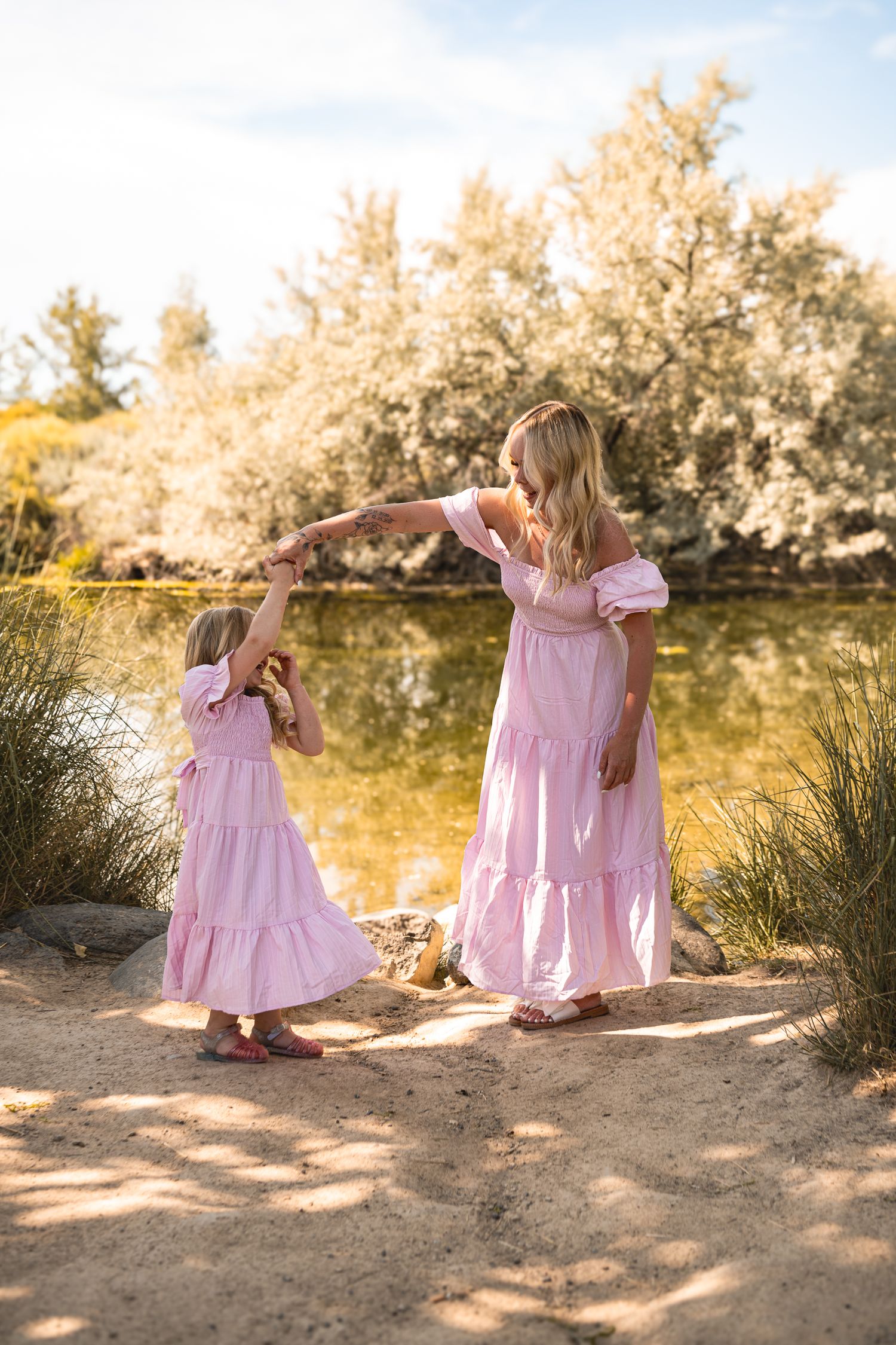 Two people in matching pink dresses dance together at sunset near a desert pond.