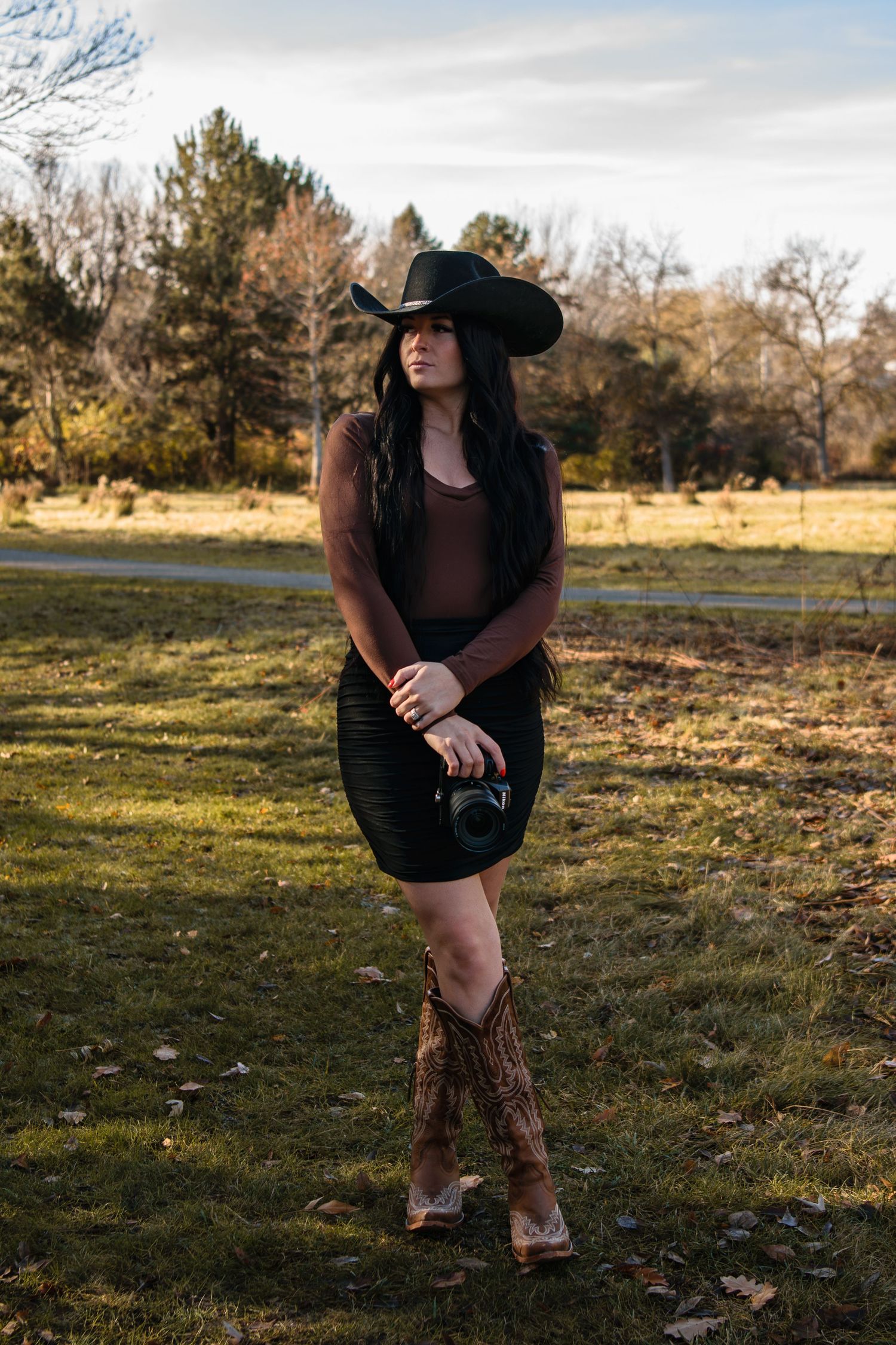 A series of outdoor portraits in warm sunlight showing a figure in a black dress and cowboy boots posing in a grassy field.