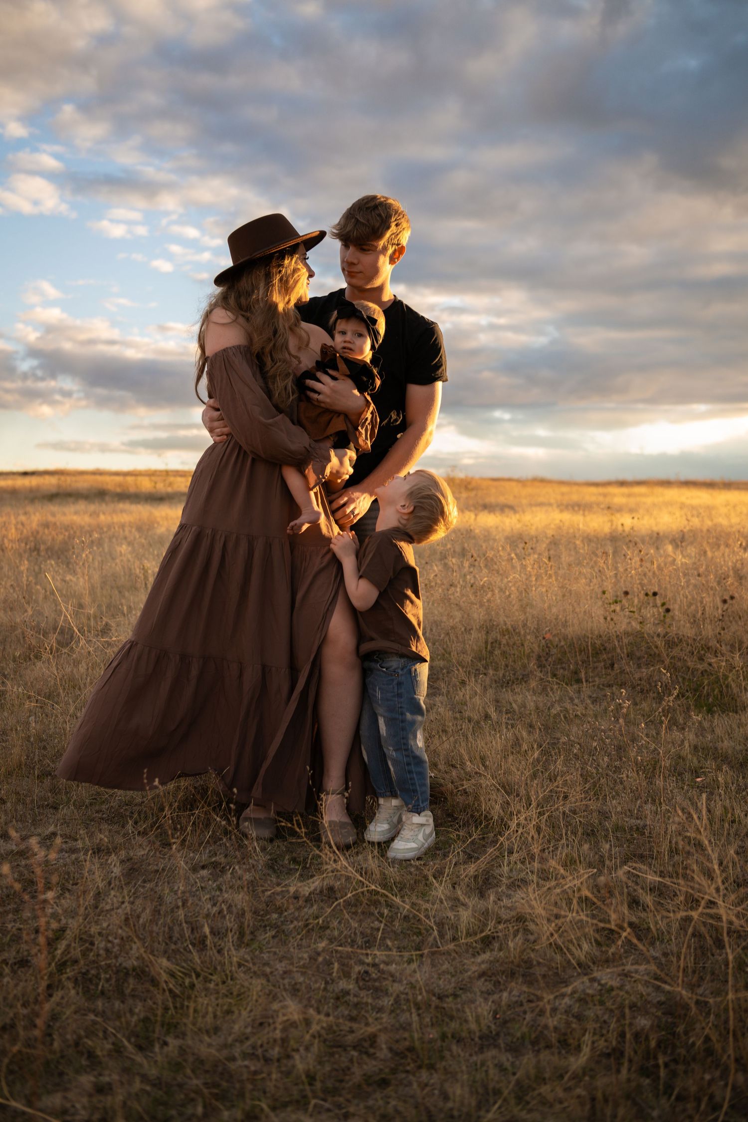 A parent and child share a tender moment in a golden wheat field at sunset as clouds drift overhead.