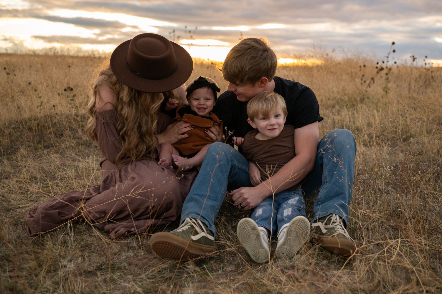 A couple sits close together in a golden field at sunset, creating an intimate and romantic autumn scene.