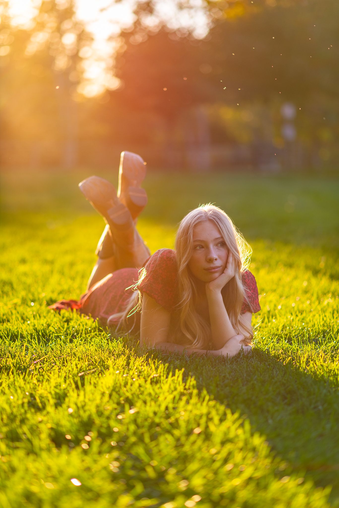 Person relaxing on lush green grass during golden sunset with warm bokeh lighting effects in background.