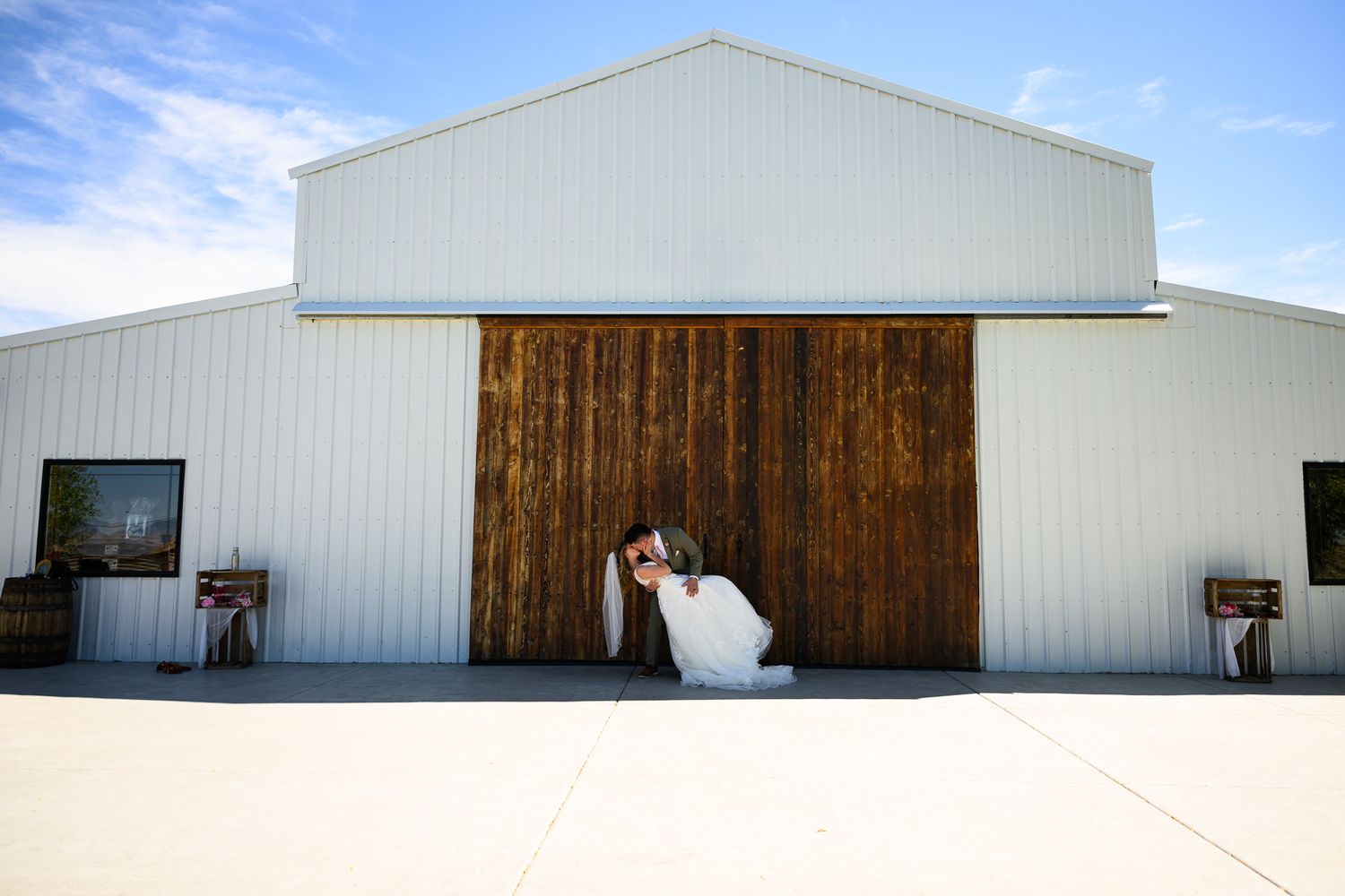 Bride and groom sharing a romantic kiss in front of rustic barn doors at an outdoor wedding venue.