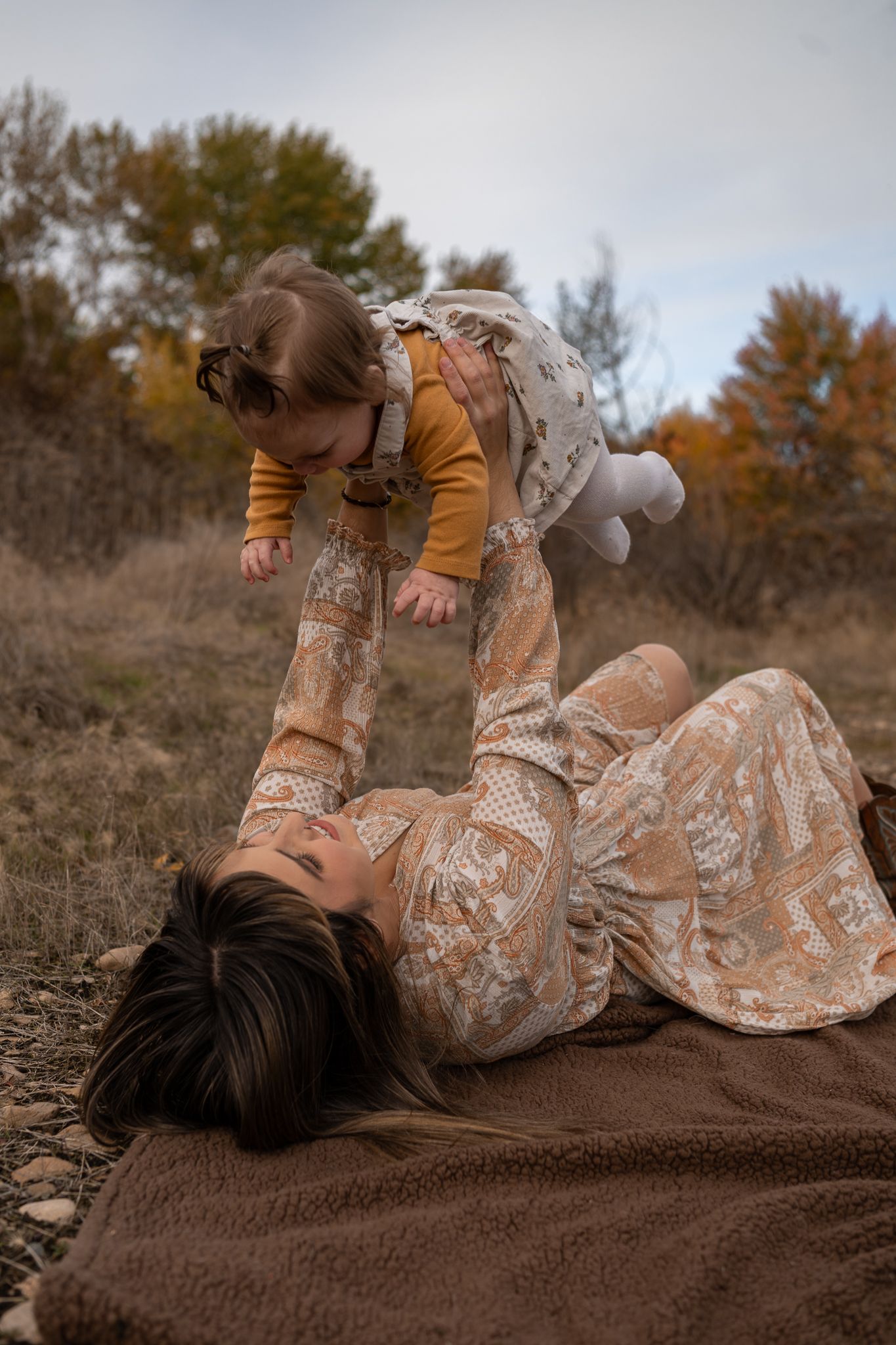 A person in a vintage lace dress lies gracefully on a brown blanket outdoors during autumn.