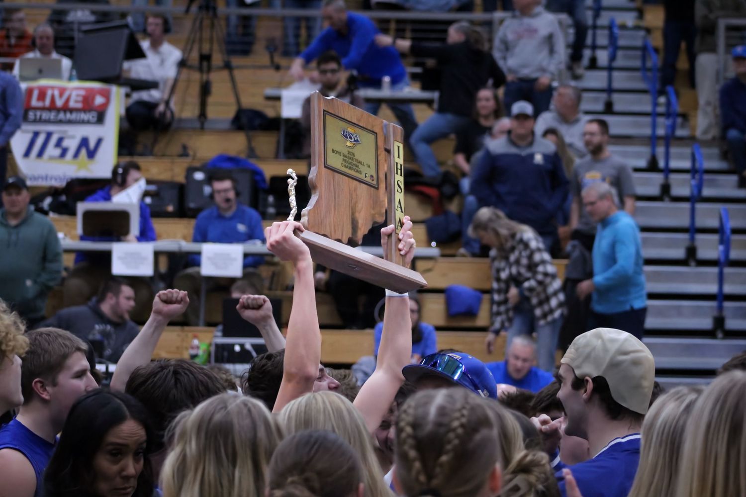 The 2026 IHSAA 1A Regional Trophy being held above a basketball crowd that rushed the court.
