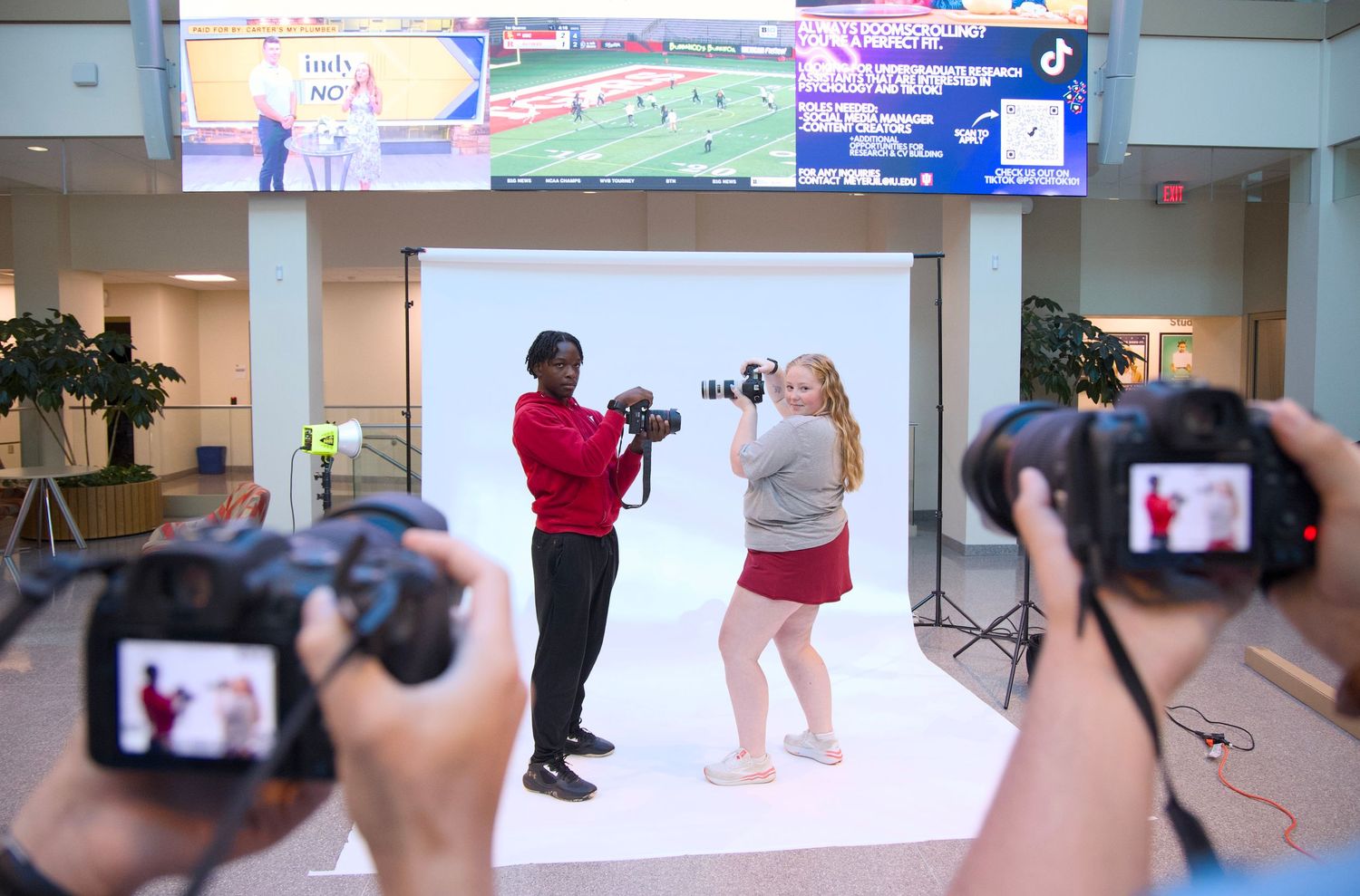 Photographers taking photos of other photographers on a white backdrop in The Media School commons at Indiana University Bloomington.