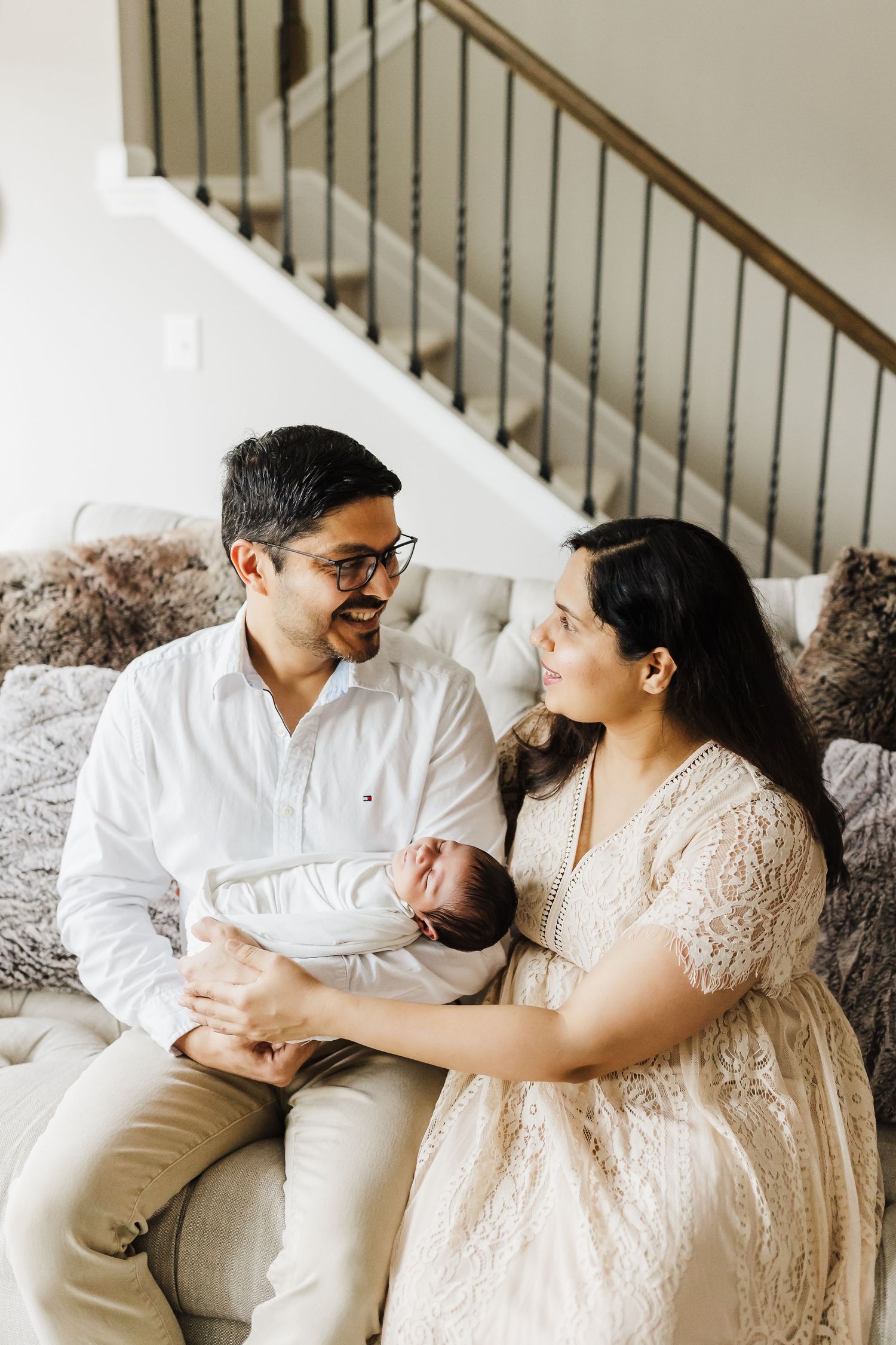 A couple in light colored outfits share intimate moments while sitting on a couch in a series of candid photos.
