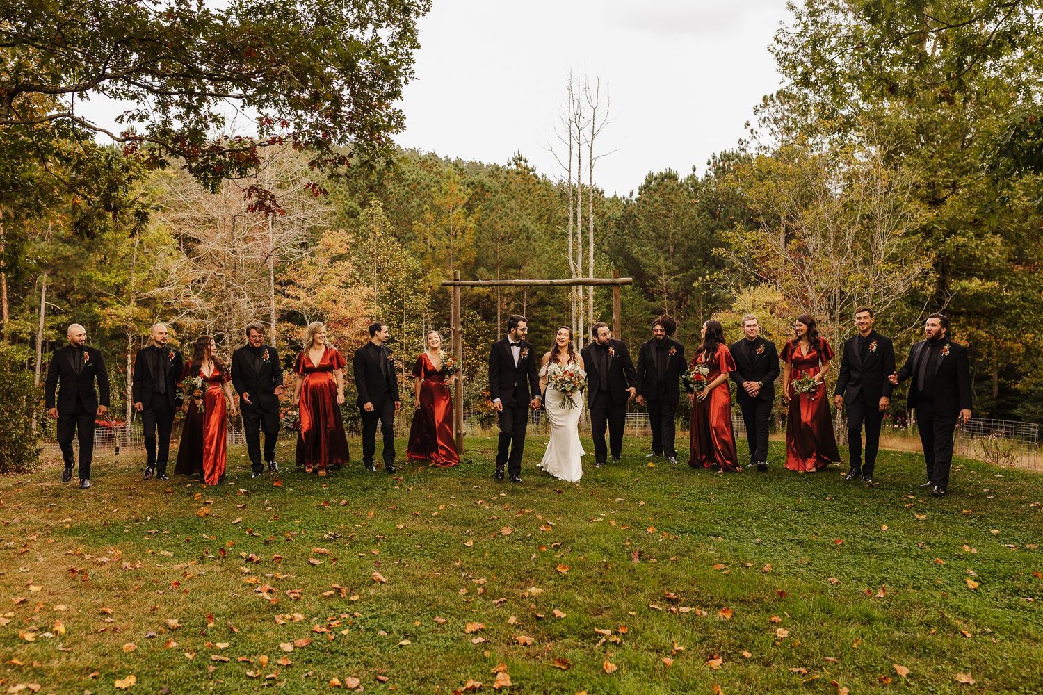 Wide panoramic shot of wedding guests lined up outdoors on a grassy hillside during autumn.