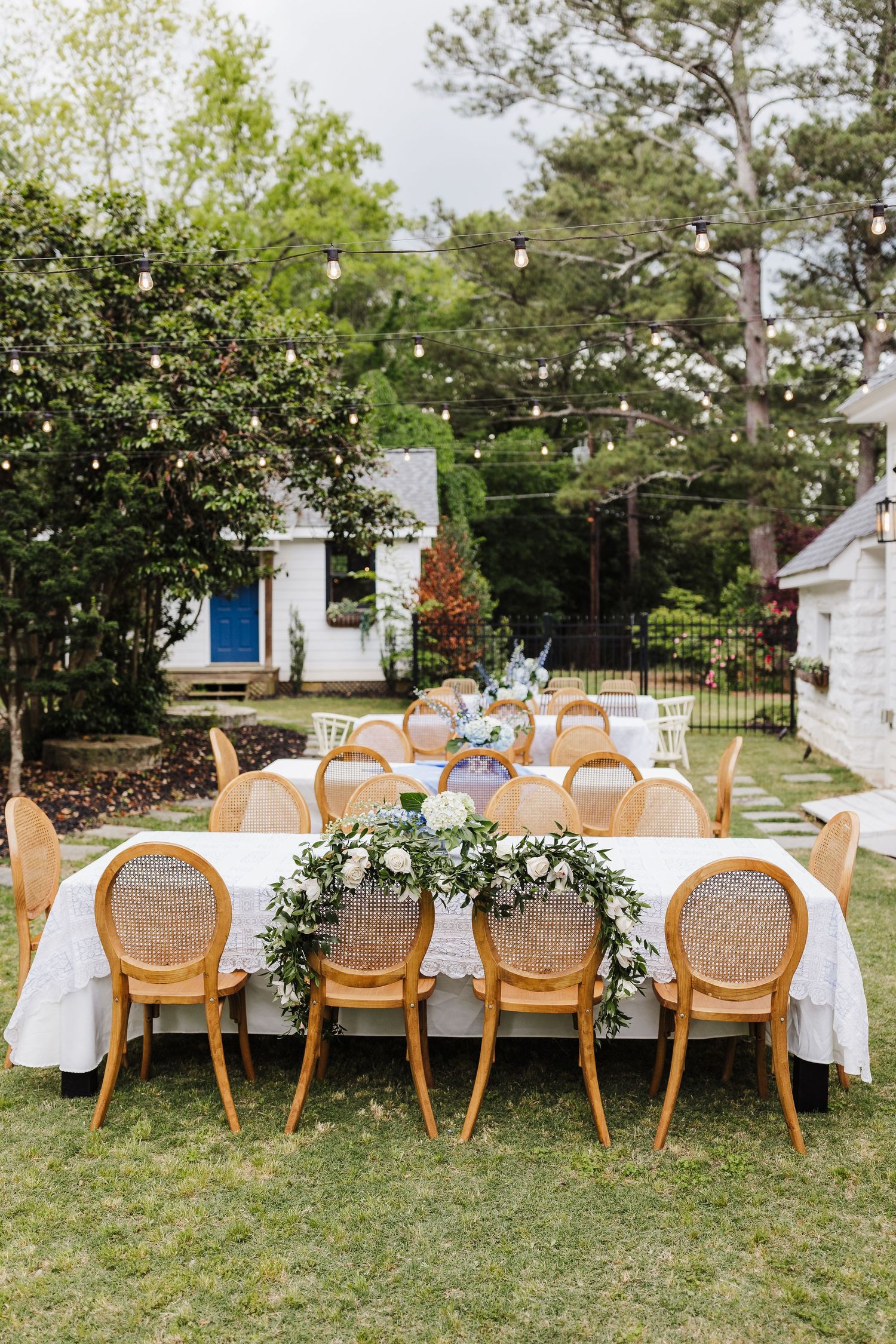 Elegant outdoor wedding reception setup with cane chairs and white linens under string lights.
