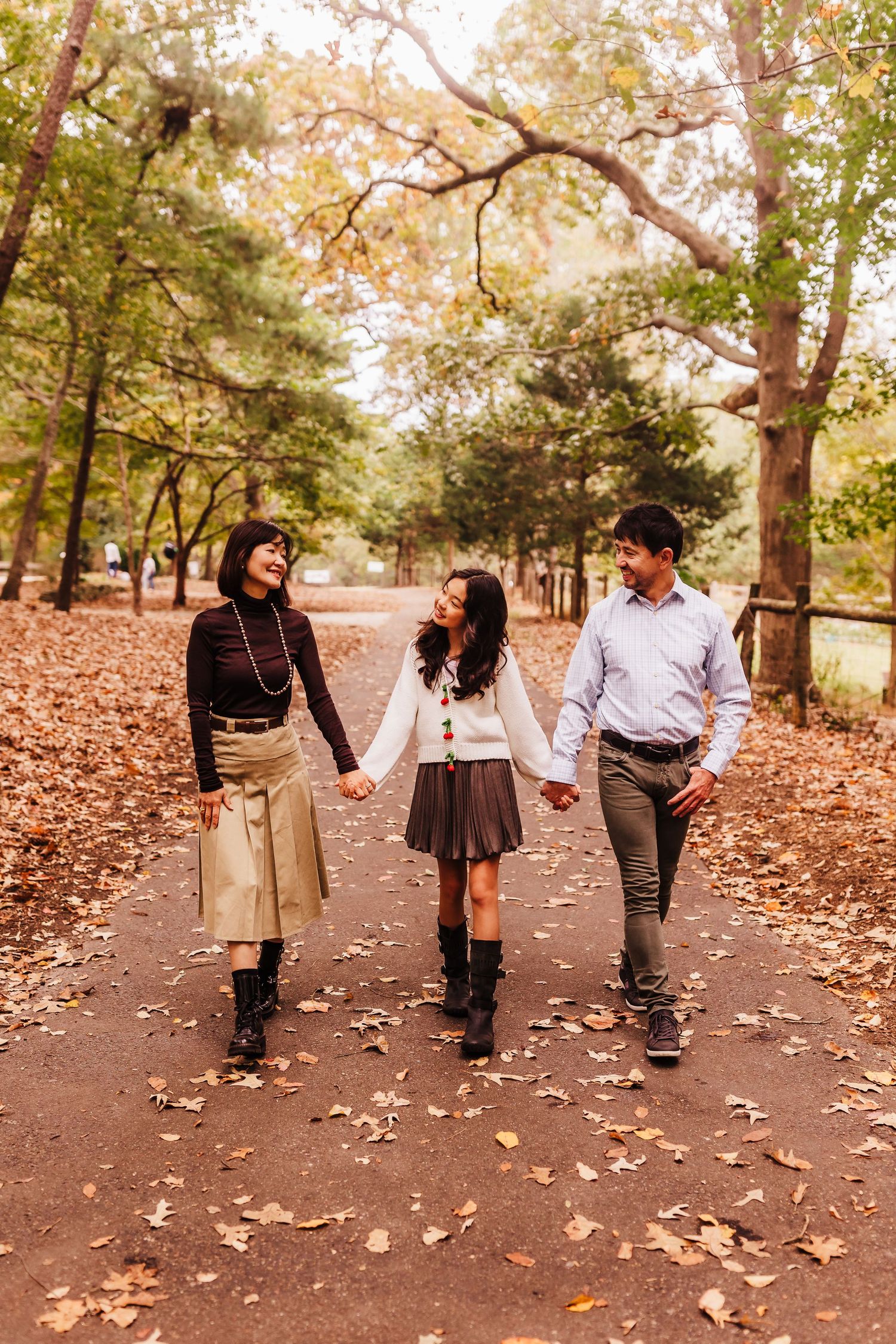 A family walking together on a path covered in fallen autumn leaves during a sunny fall day at McDaniel Farm Park