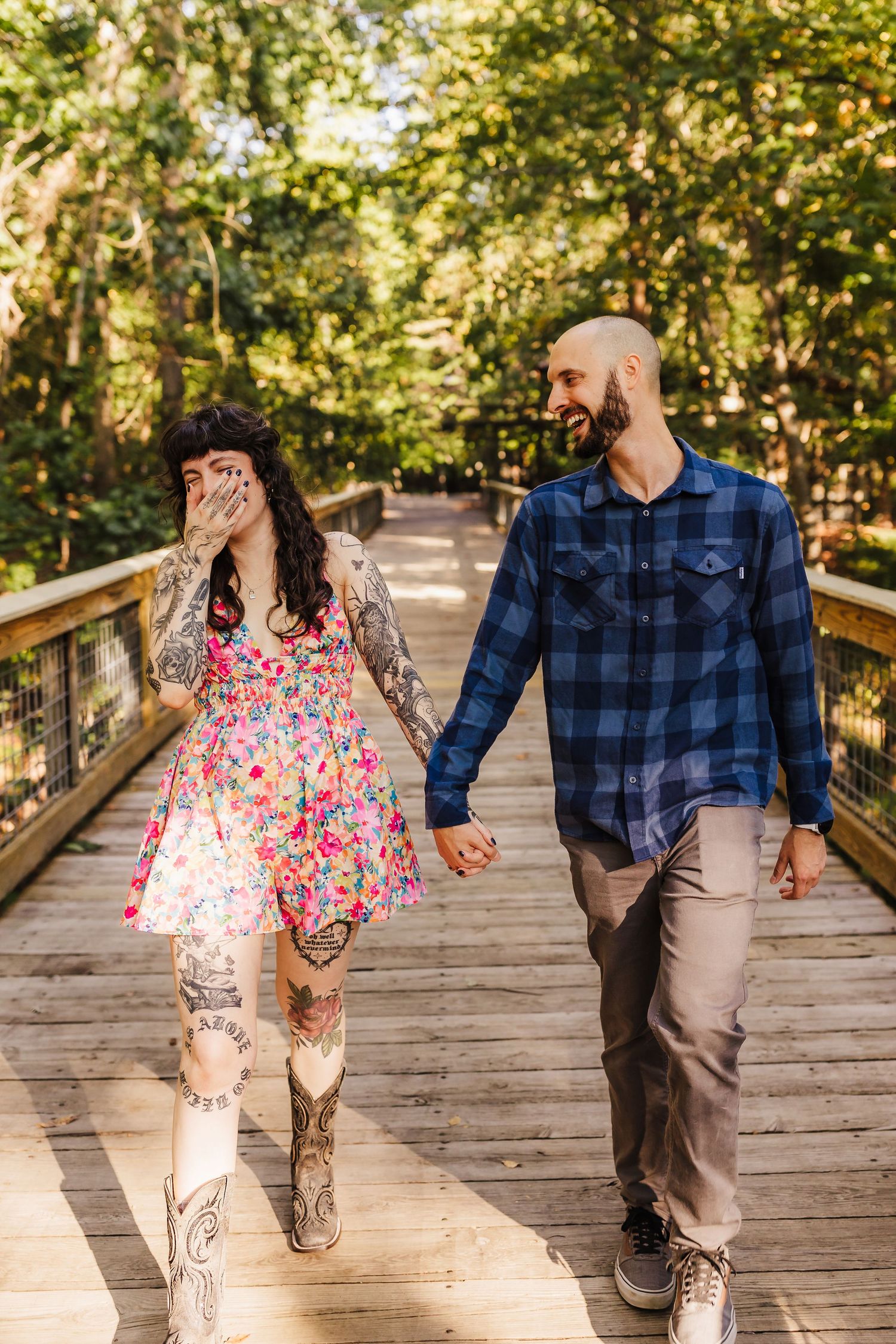 Couple holding hands while walking on a wooden bridge through lush forest.