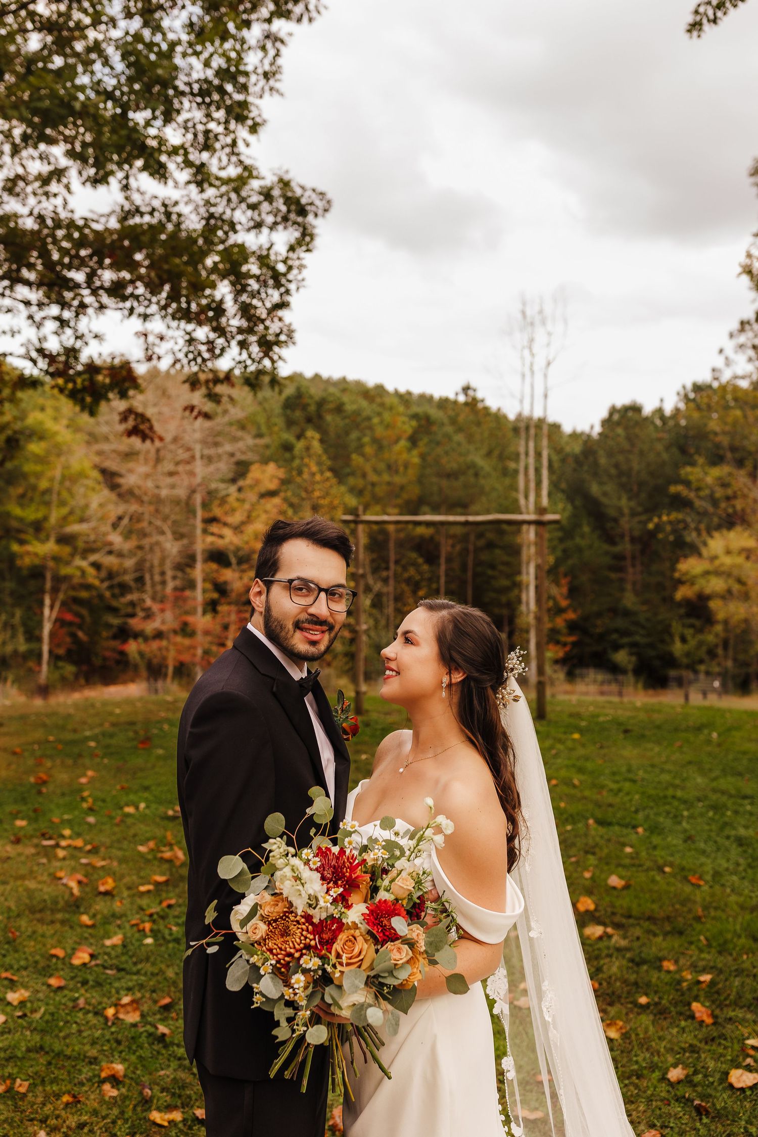 A couple shares a joyful moment in an autumn field with colorful bouquet and wedding attire.