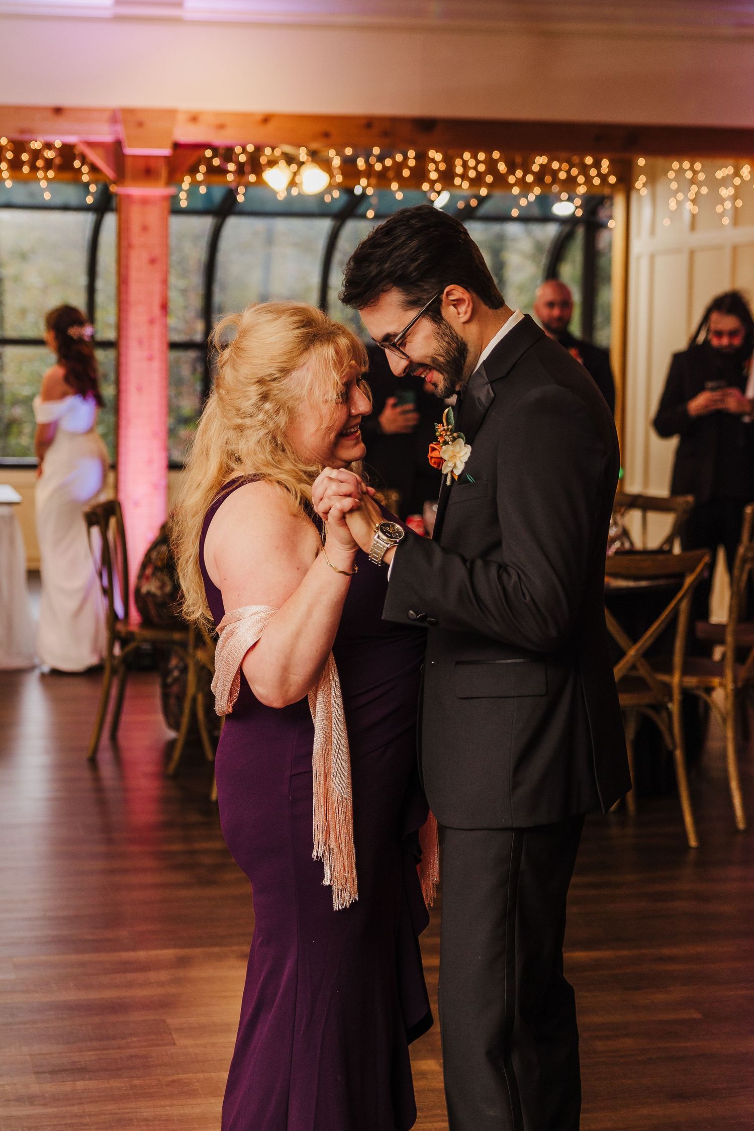 Couples dancing in an elegant reception hall with string lights and purple accents.