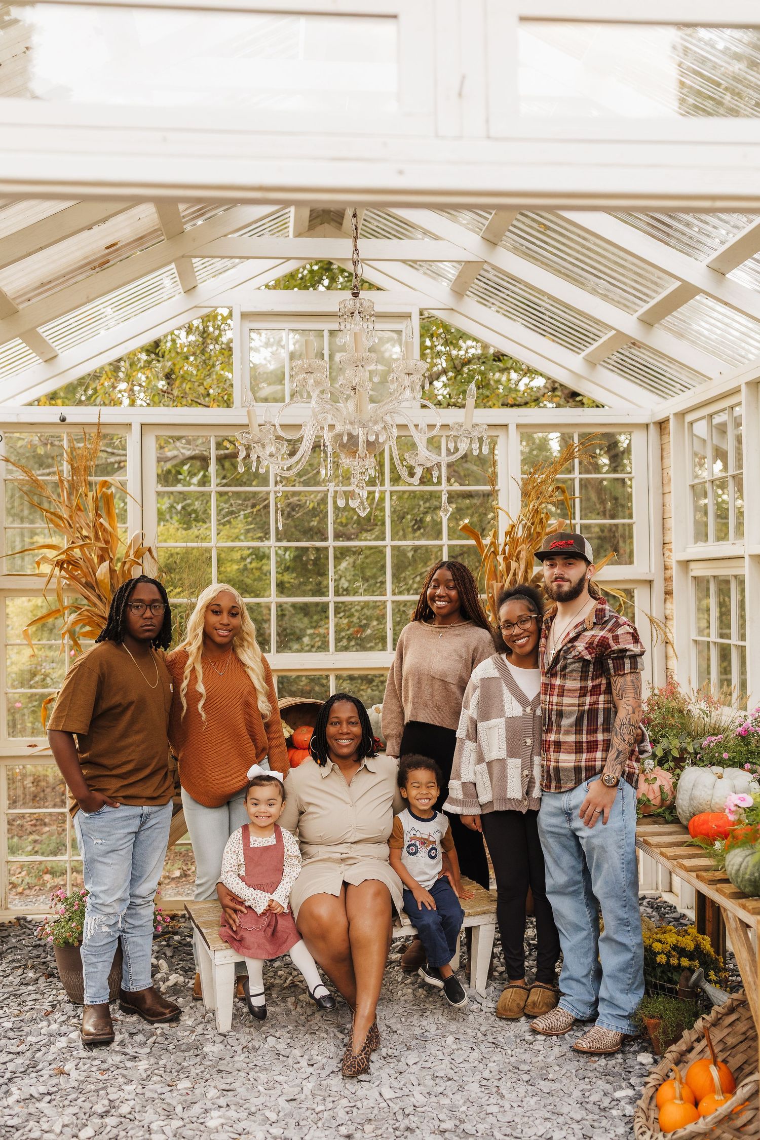 Family portrait in a glass greenhouse with fall decor, chandelier, and pumpkins during autumn season.