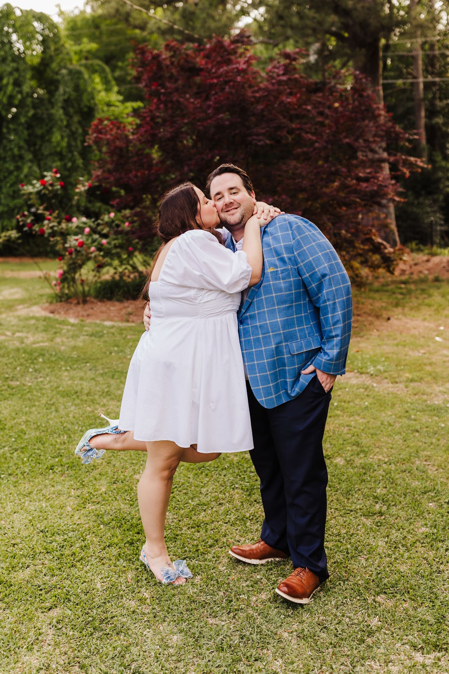 A sweet moment shared between a couple in white and blue outfits in a garden setting.