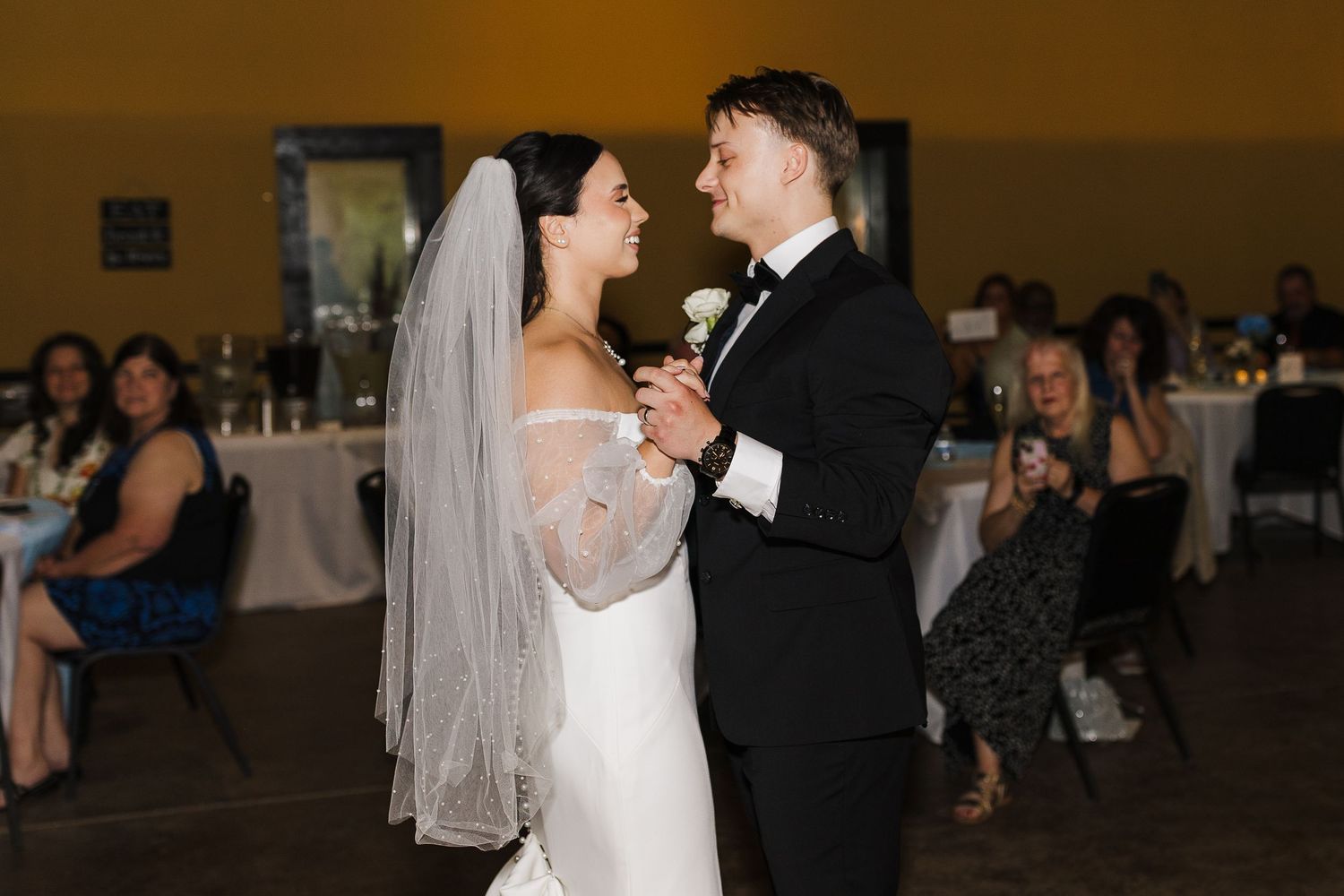 Bride and groom share their first dance at wedding reception, bride wearing white gown and veil, groom in black tuxedo.