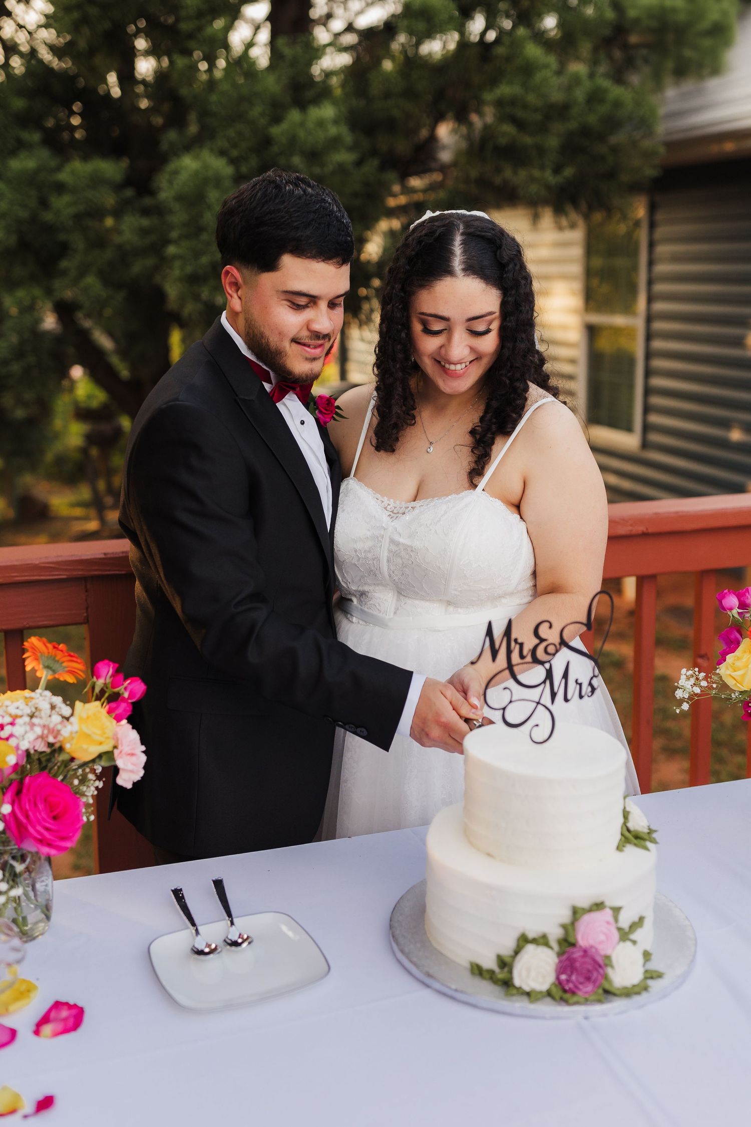 Newlyweds share a joyful moment while cutting their elegant white wedding cake with floral decorations.