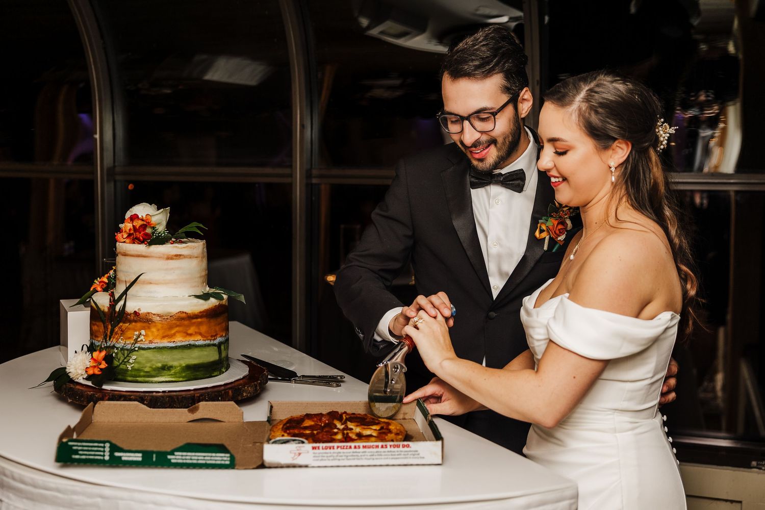 Wedding cake cutting ceremony at an indoor reception with rustic decorations and ambient lighting.