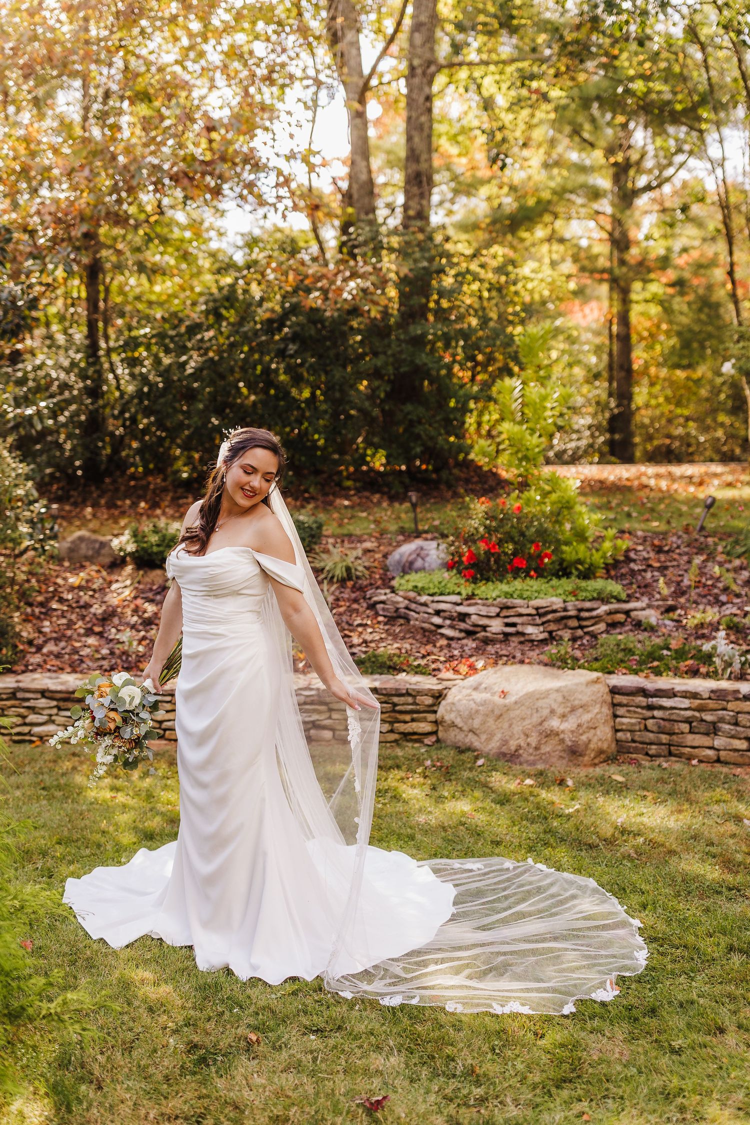 A person in a flowing white wedding dress twirls gracefully on a grassy lawn during an autumn photo session.