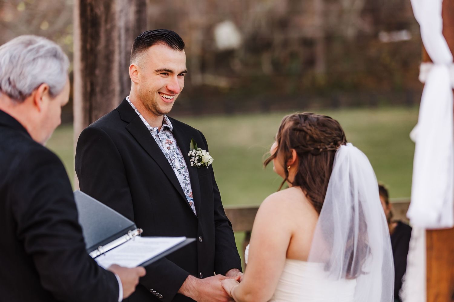 An emotional wedding ceremony moment with a couple exchanging vows under an outdoor arch.