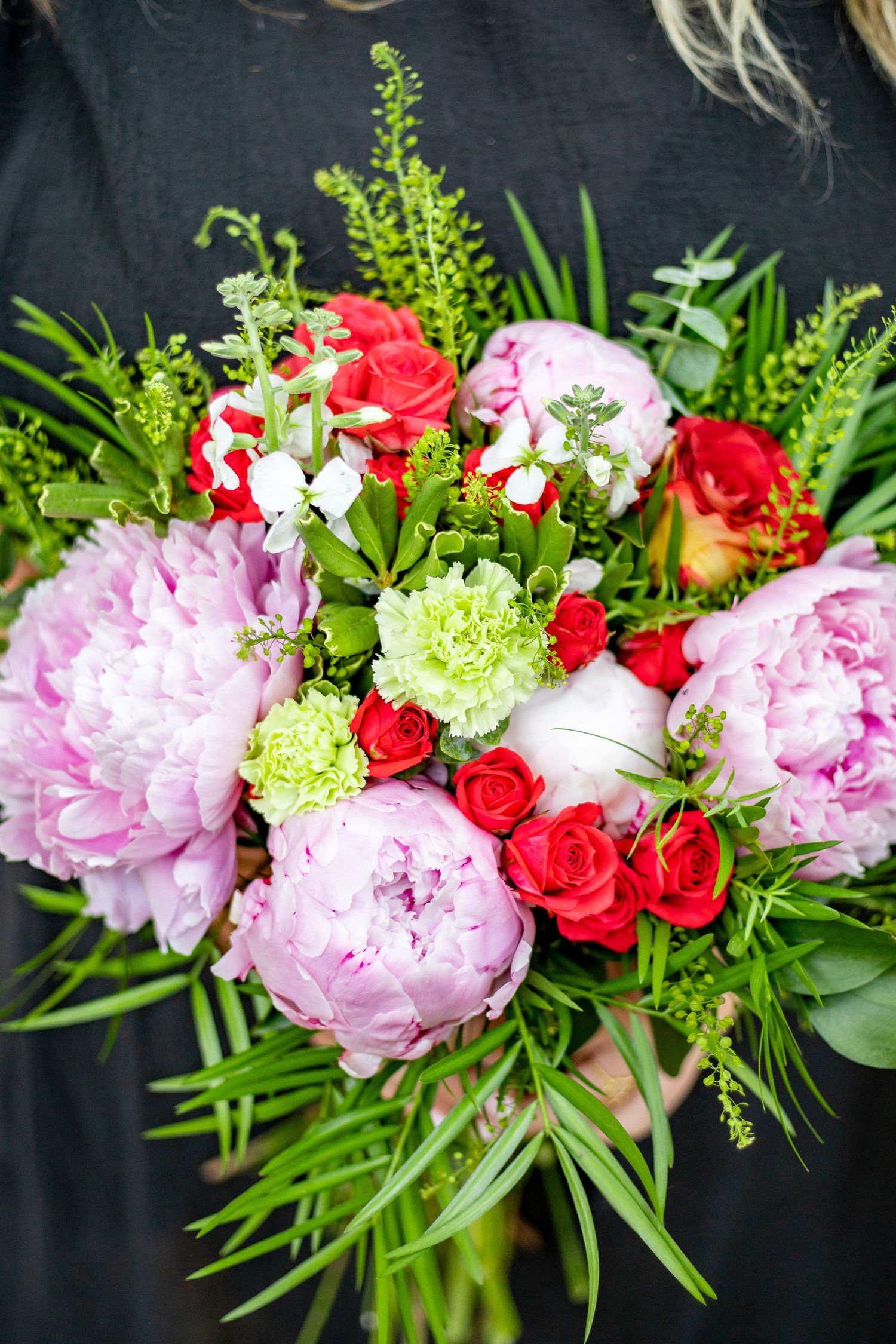 Stunning floral arrangement featuring pink peonies, red roses, and green foliage against dark background.
