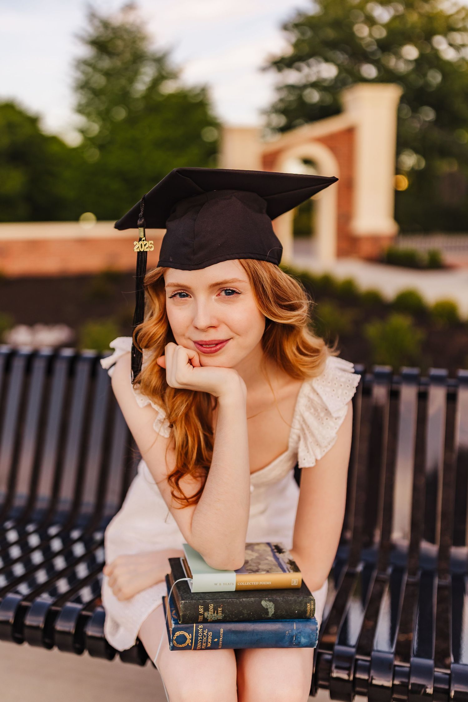 University of North Georgia graduation portrait in Dahlonega featuring a graduate wearing a cap and gown while seated on a bench with books.